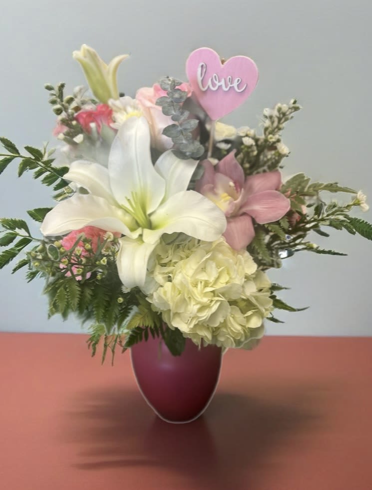 Bouquet of white lilies and pink flowers in a purple vase with a pink heart pick