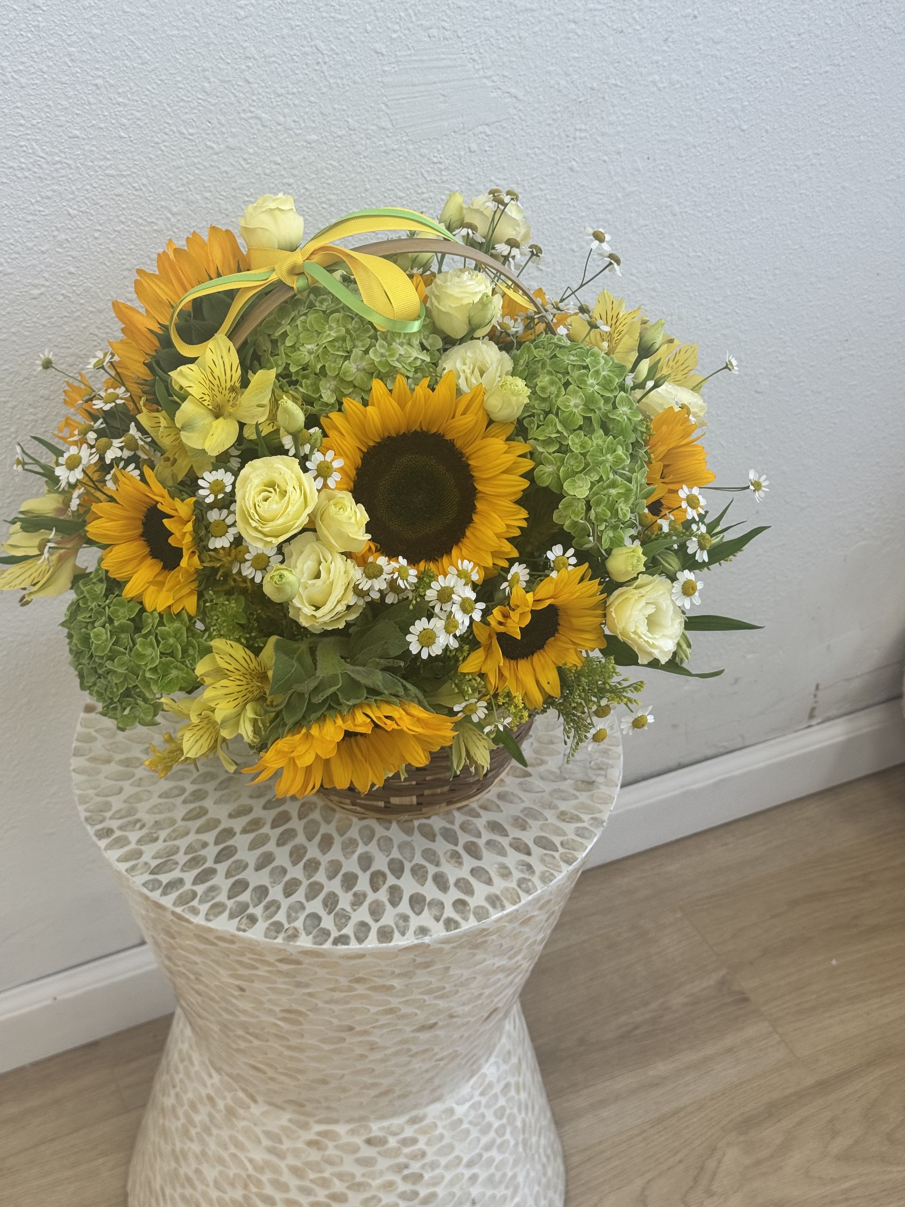 Basket arrangement of sunflowers, pale roses, and green hydrangeas with a yellow ribbon