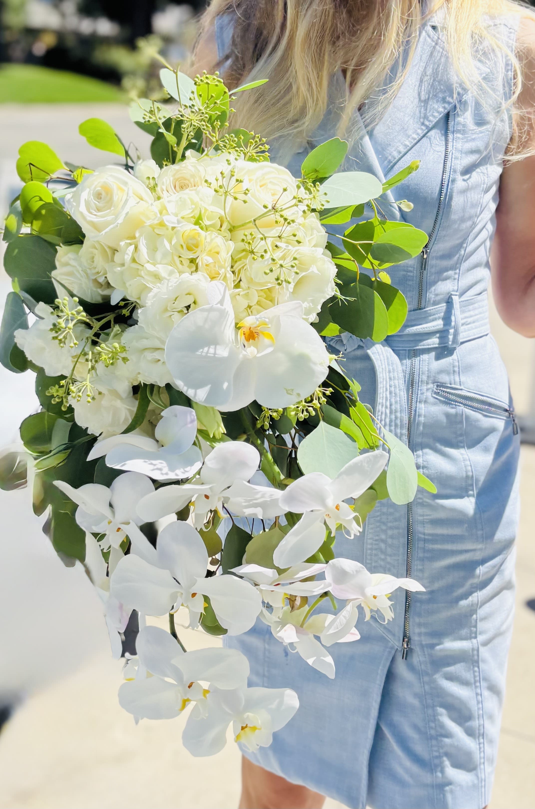 White bouquet with roses and orchids held by a person in a light blue dress