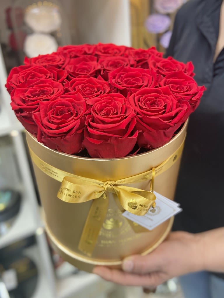 Round gold hat box filled with tightly packed red roses and tied with a yellow satin ribbon
