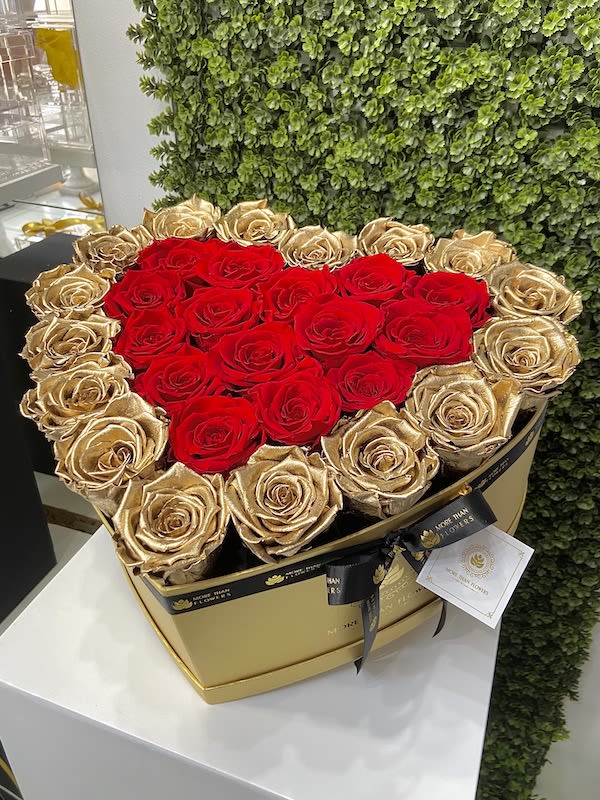 Heart-shaped gold box filled with red and gold roses and tied with a black ribbon