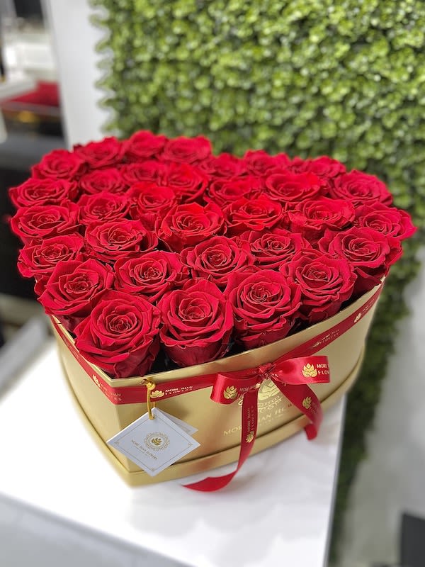 Heart-shaped gold box filled with red roses and tied with a red ribbon and tag
