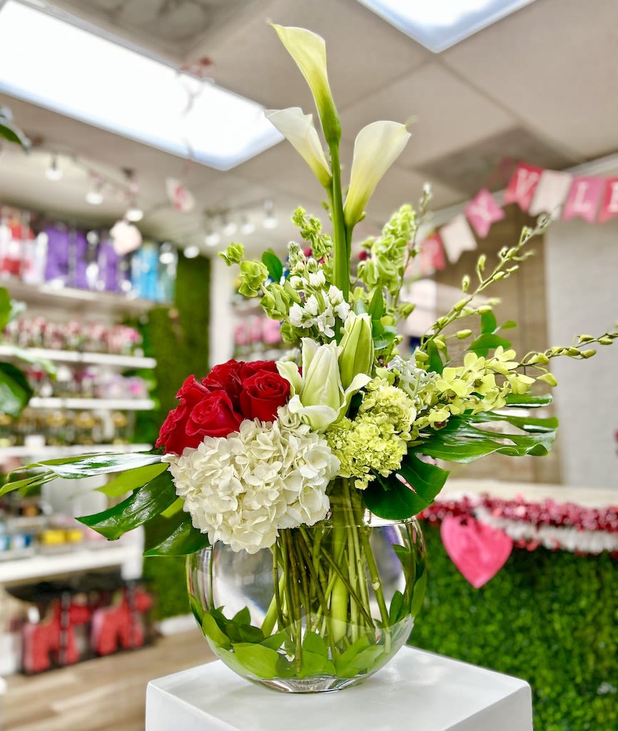 Low glass bowl of red roses, white hydrangeas, calla lilies and green blooms in an asymmetrical arrangement