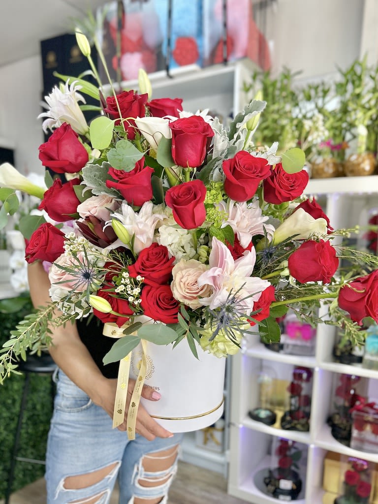 Large arrangement of red roses with pale pink and white lilies in a round white hatbox container
