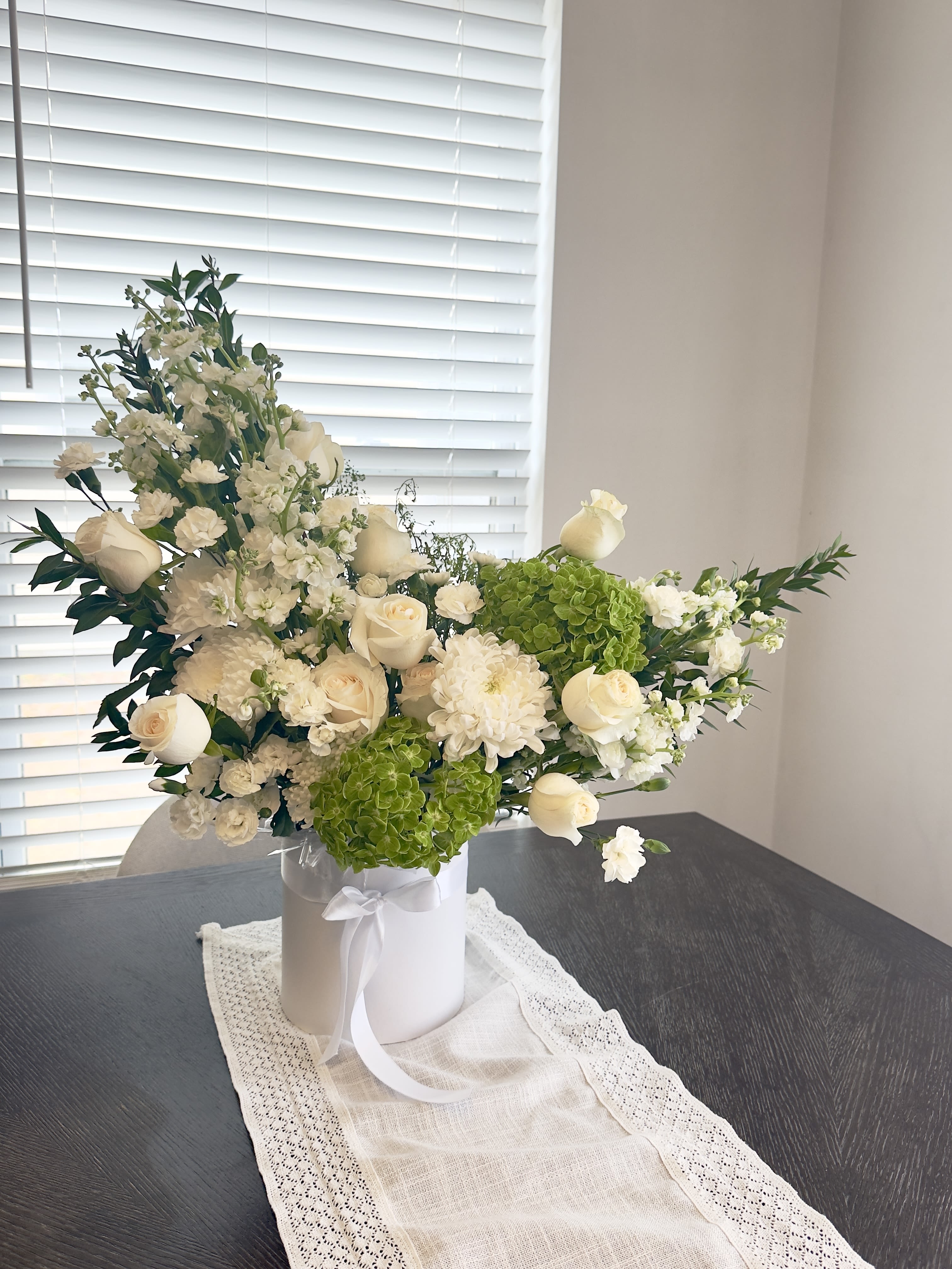 White floral arrangement in a white hatbox with green hydrangeas and roses