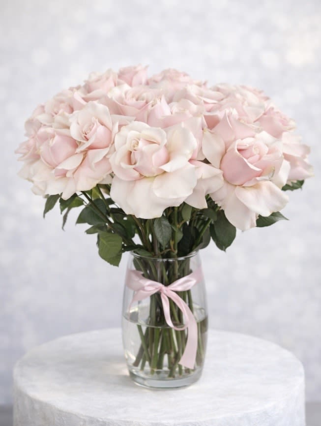 Pale pink roses arranged in a clear glass vase with a pink ribbon
