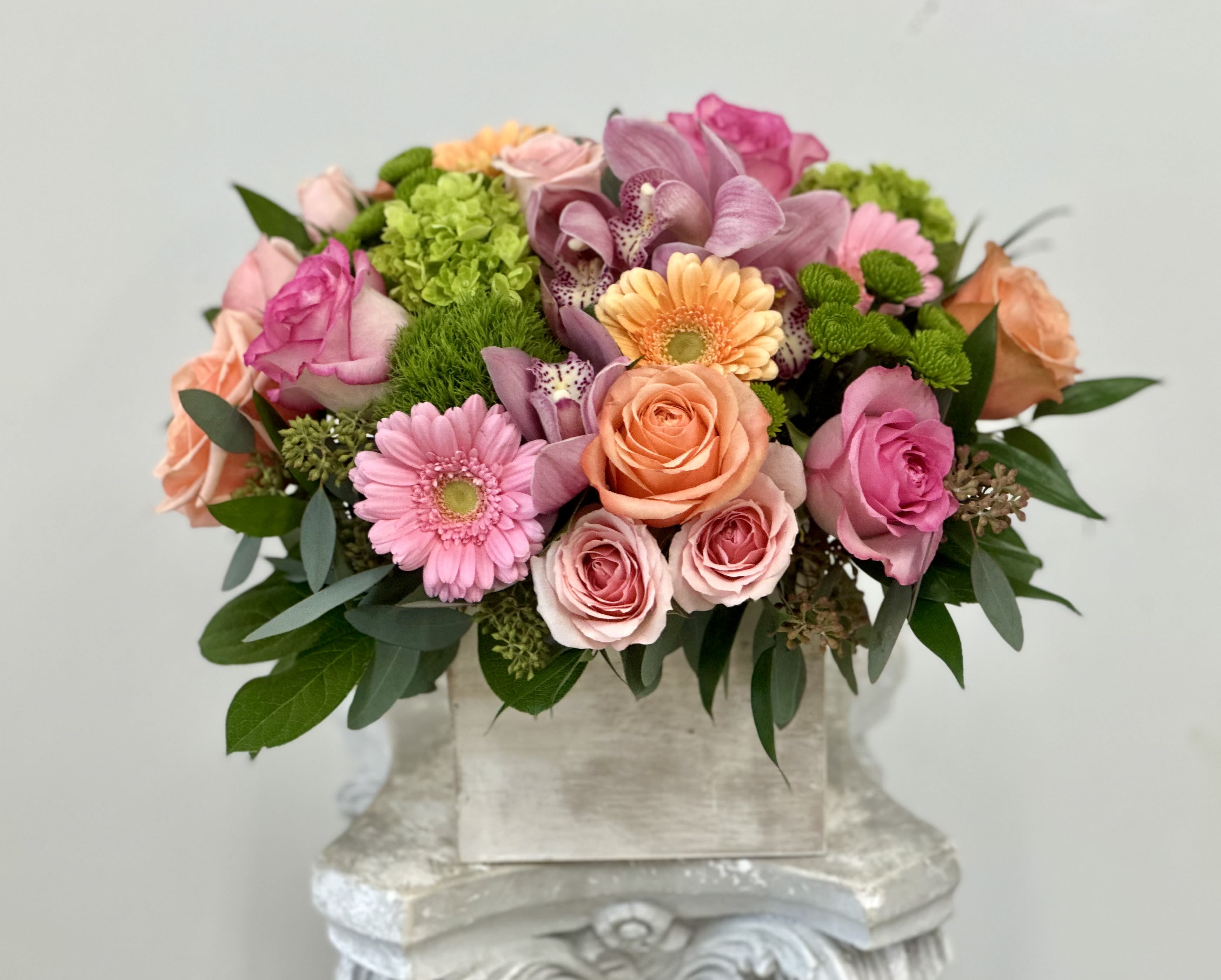 Low arrangement of pink and peach roses, gerbera daisies, orchids and mums in a rustic box vase