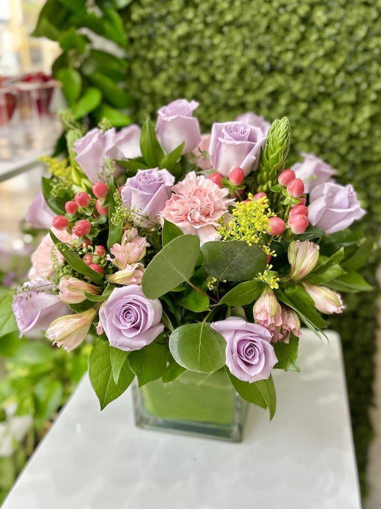 Lavender roses and pink carnations with berries in a square glass vase