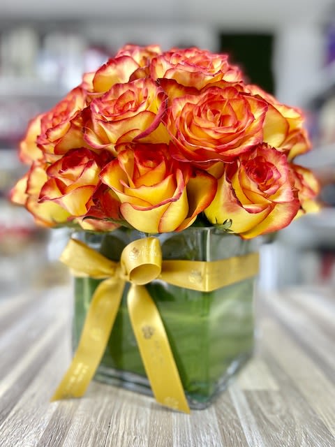 Compact bouquet of yellow roses with red edges in a square glass vase tied with a yellow ribbon