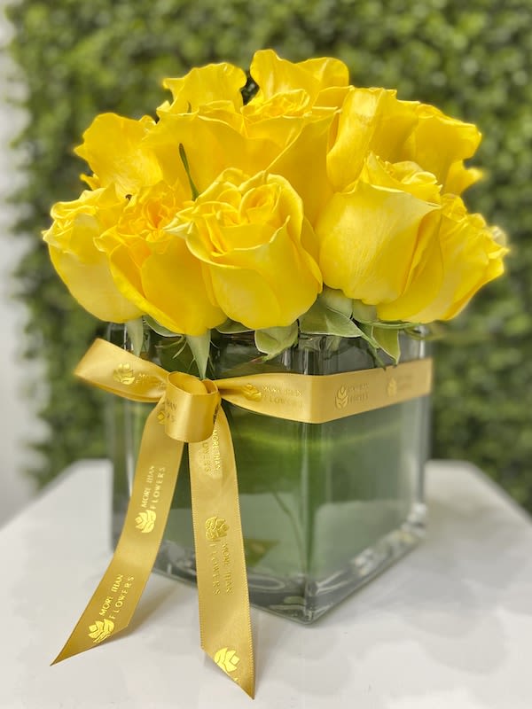 Compact arrangement of bright yellow roses in a clear cube vase with a yellow ribbon bow