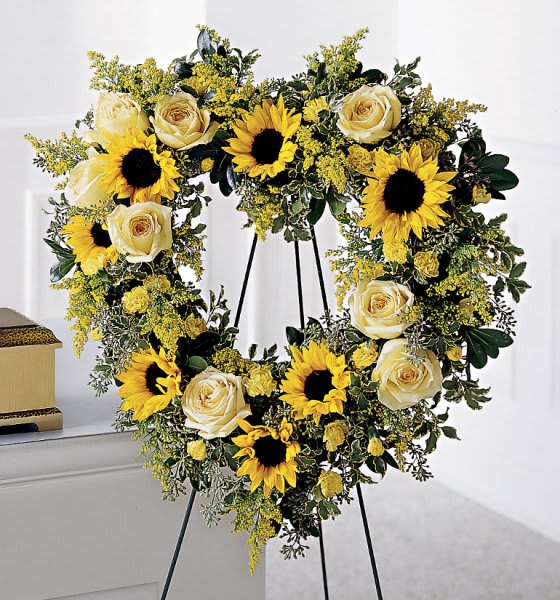 Heart-shaped floral wreath with sunflowers and cream roses on a stand