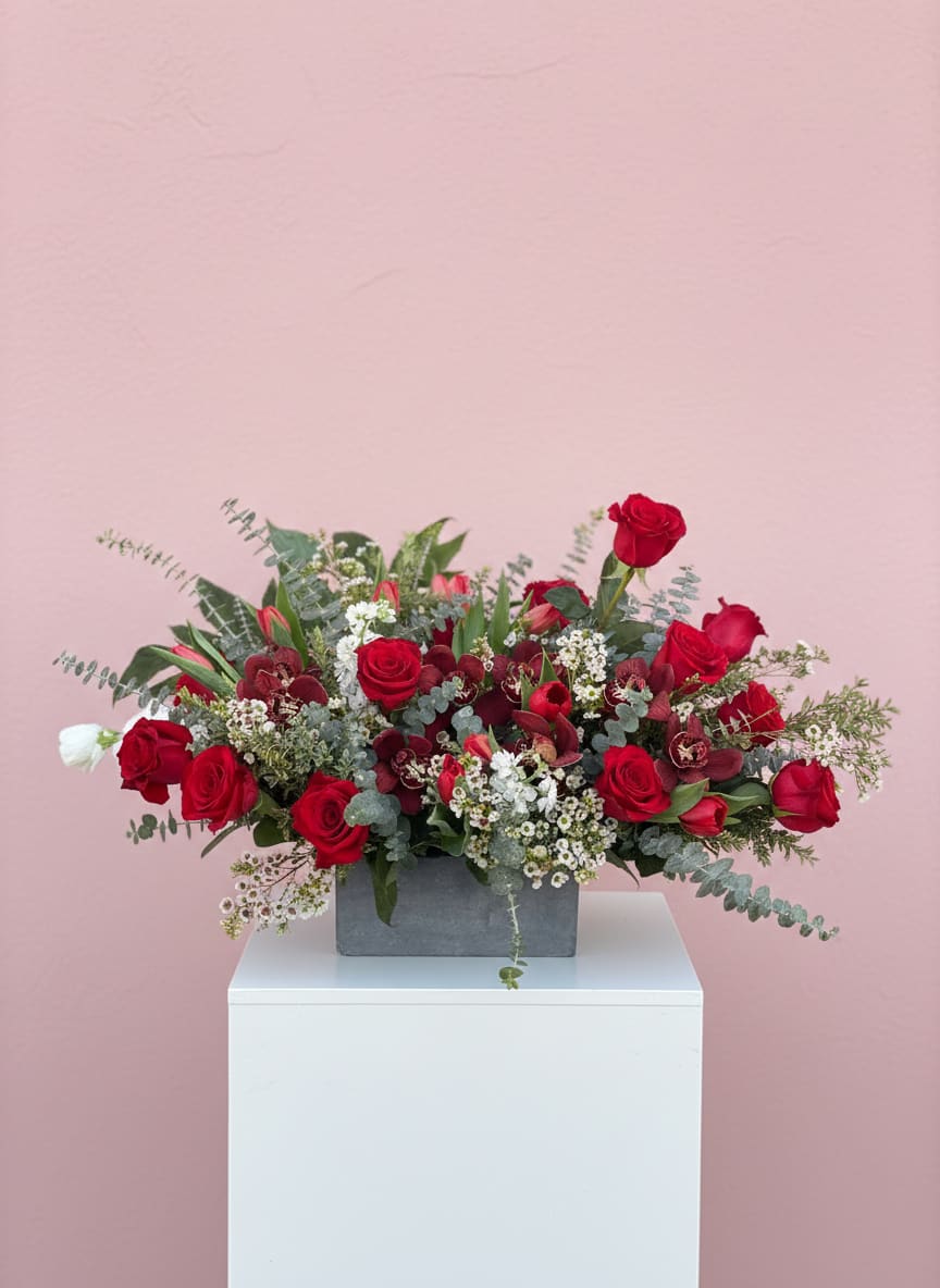 Red roses arranged in a gray rectangular vase with white filler flowers