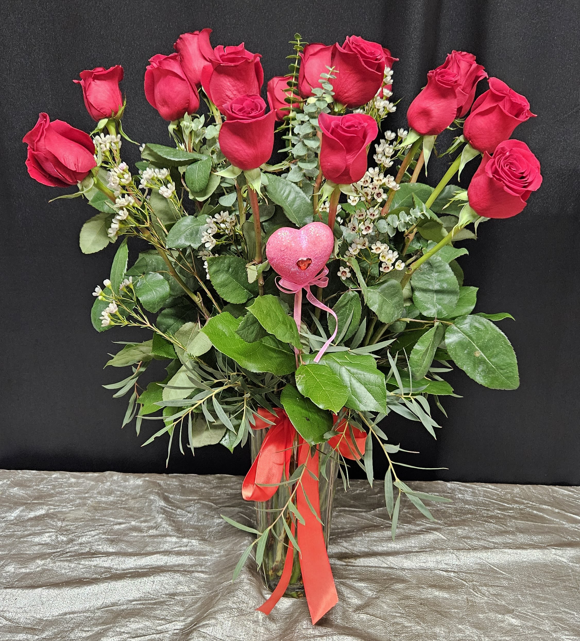 Bouquet of red roses with greenery in a clear glass vase and pink heart pick