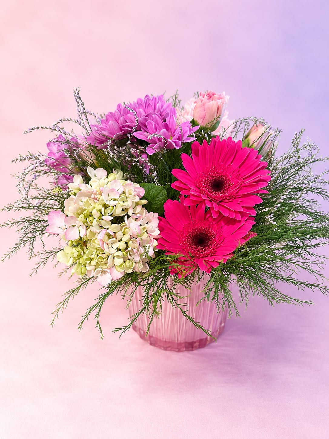 Pink Petal Glow - Soft, feminine, and full of vibrant charm, Pink Petal Glow features bold hot pink gerbera daisies paired with delicate hydrangea, soft pink blooms, and airy garden greenery for a fresh, romantic look. Layers of texture and shades of pink create a cheerful yet elegant arrangement that feels both modern and whimsical.