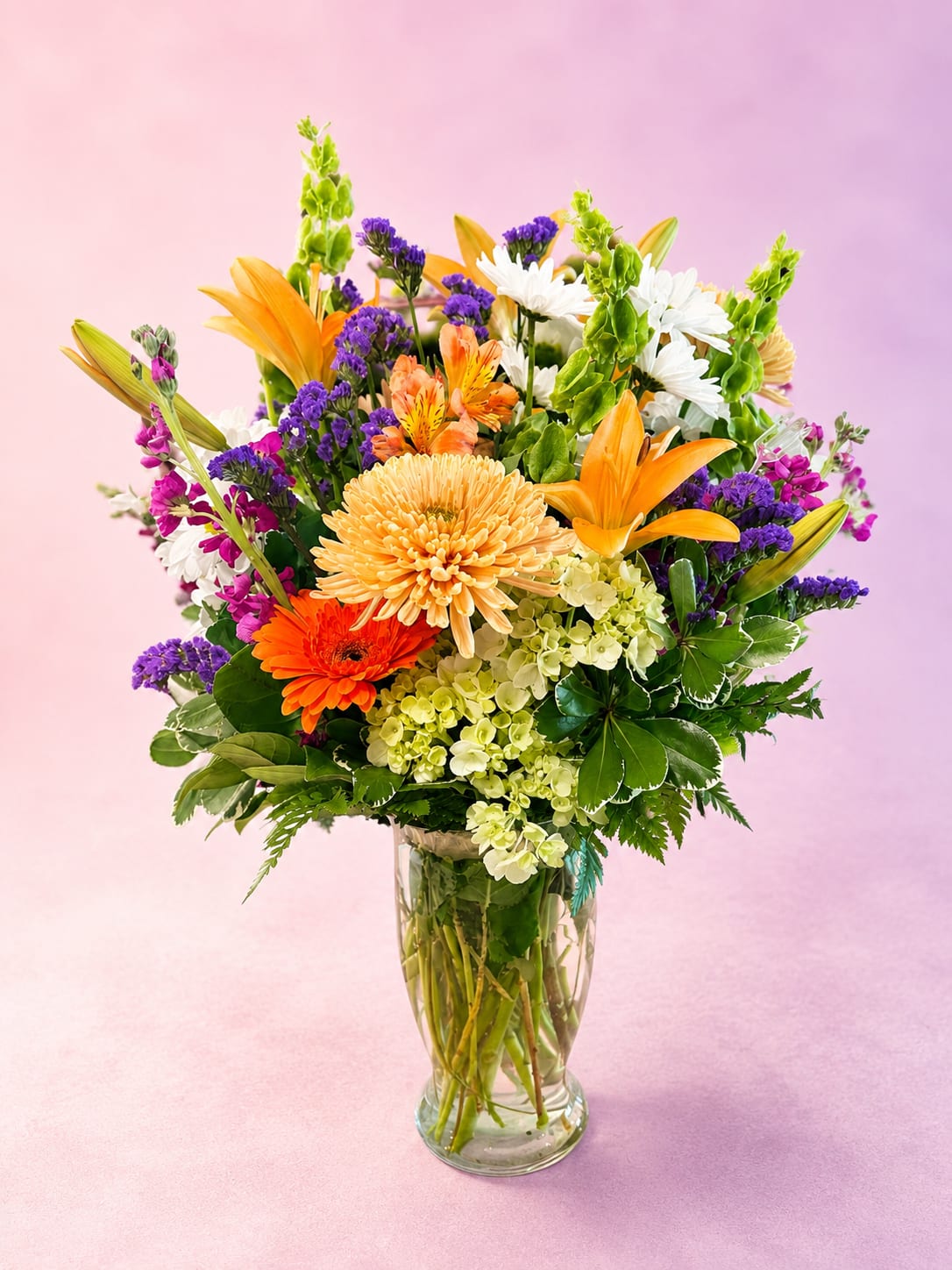 Citrus Garden - Bright, fresh, and bursting with cheerful color, Citrus Garden blends vibrant orange lilies and gerbera daisies with soft hydrangea, delicate stock, cheerful daisies, and rich purple accents for a lively garden-inspired design. Full of texture, movement, and seasonal beauty, this arrangement brings together warm citrus tones with fresh greenery for a bold yet elegant look.