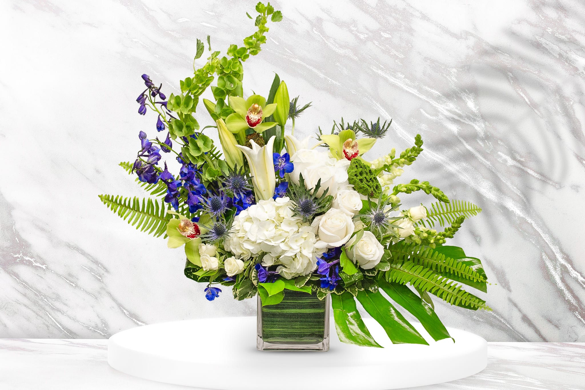 Mixed bouquet in a square glass vase with white, green, and blue flowers