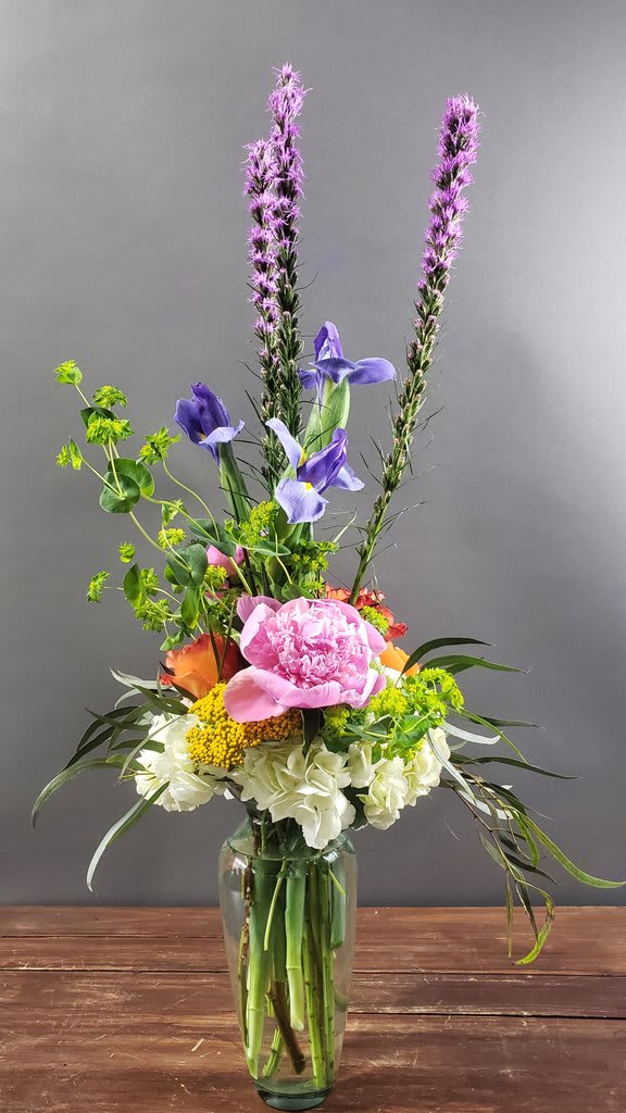 Tall mixed flower arrangement in a glass vase with pink, purple, white, and orange blooms