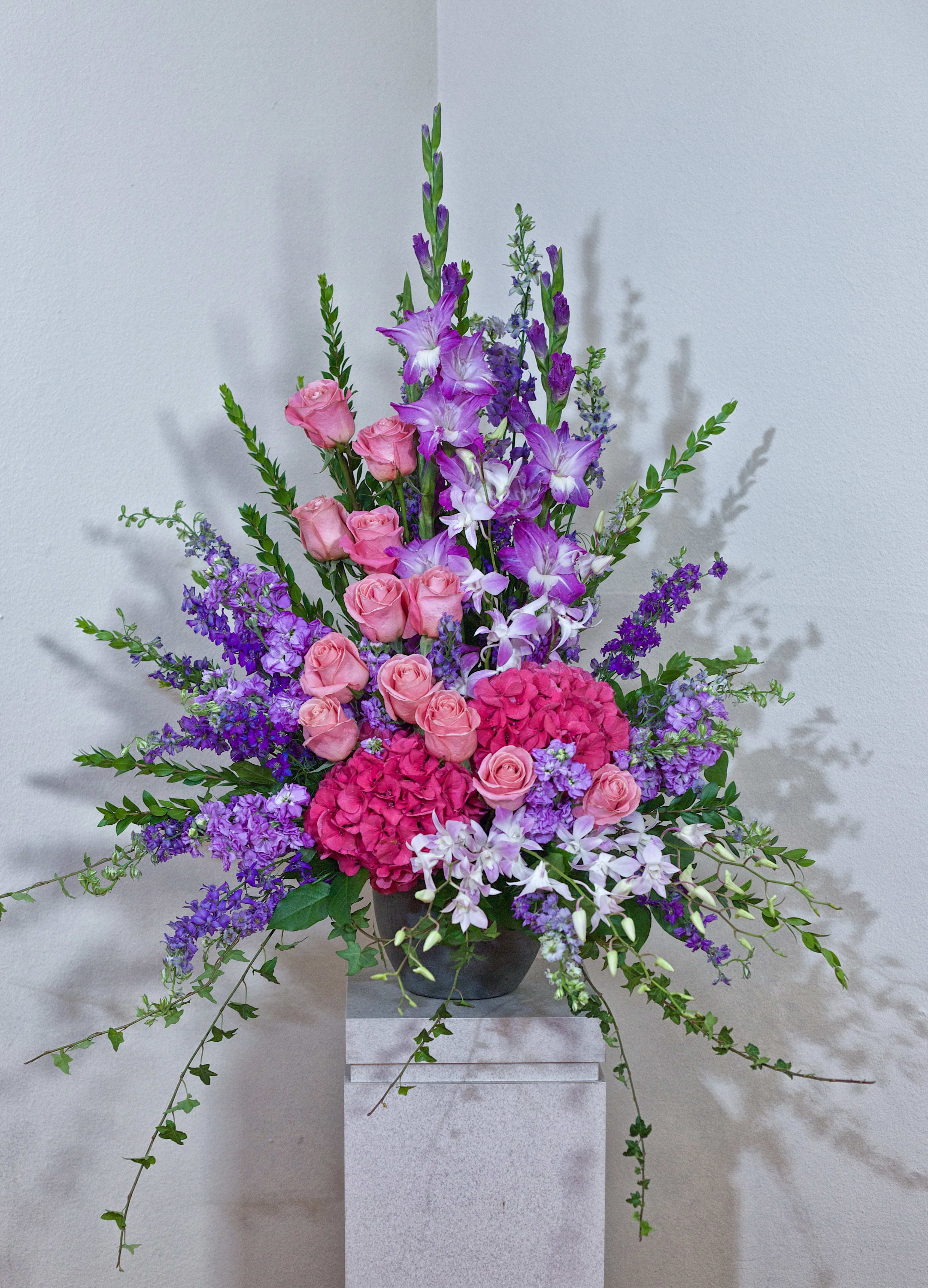 Tall arrangement of pink roses and purple flowers in a dark vase