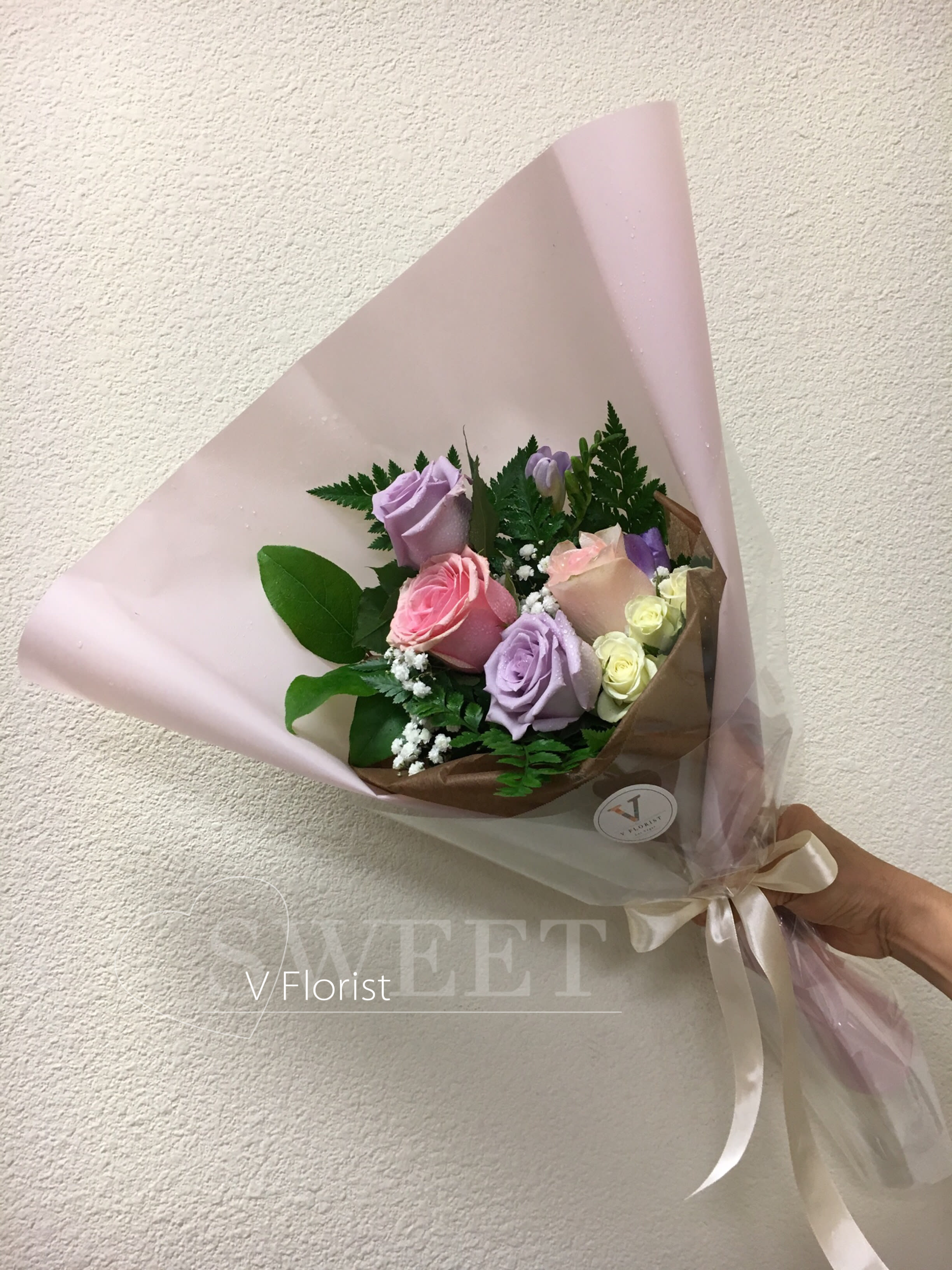 Pastel bouquet of pink and lavender roses wrapped in pink paper with a satin ribbon bow