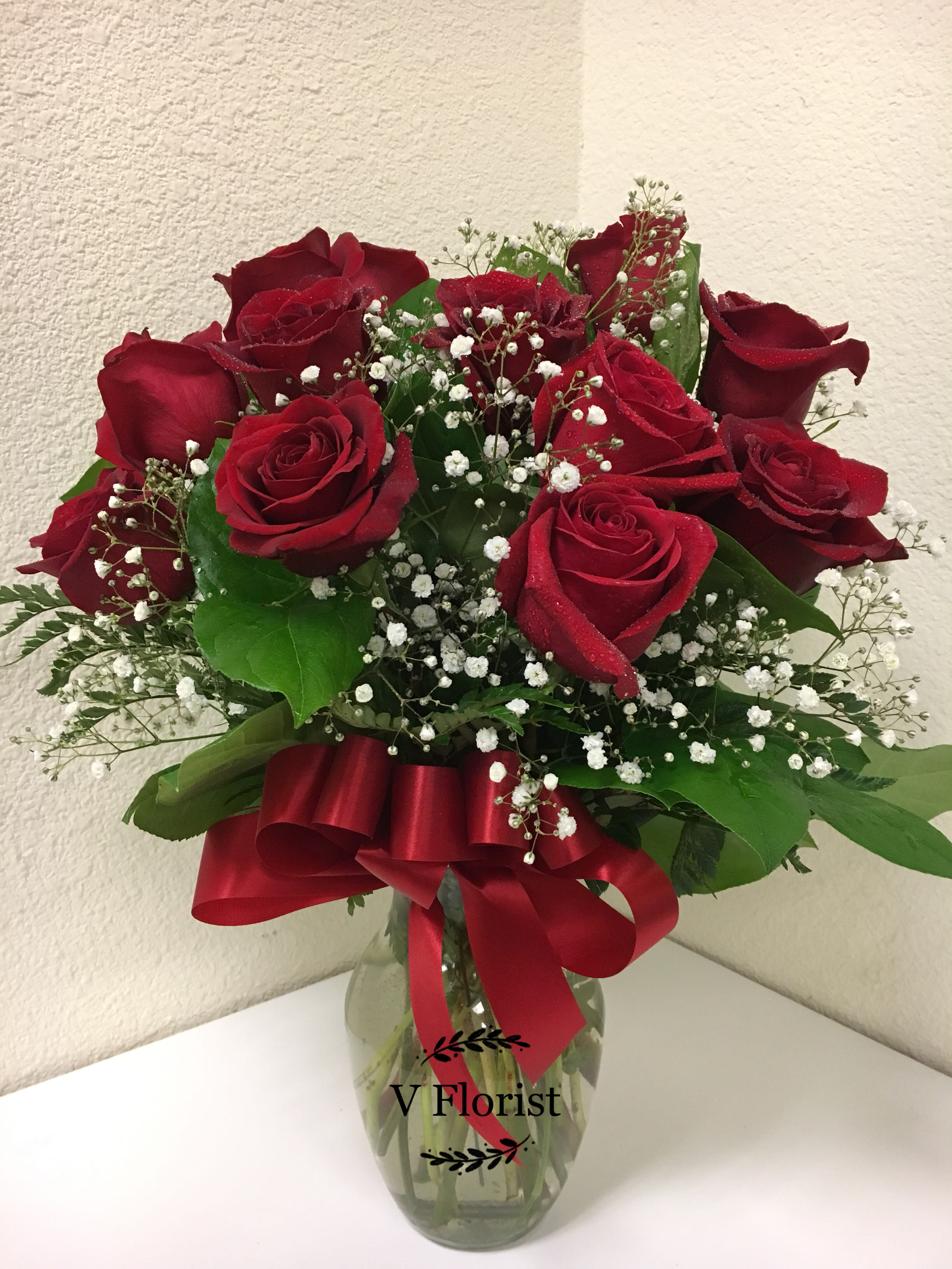 Arrangement of red roses and white filler flowers in a clear glass vase with a red bow