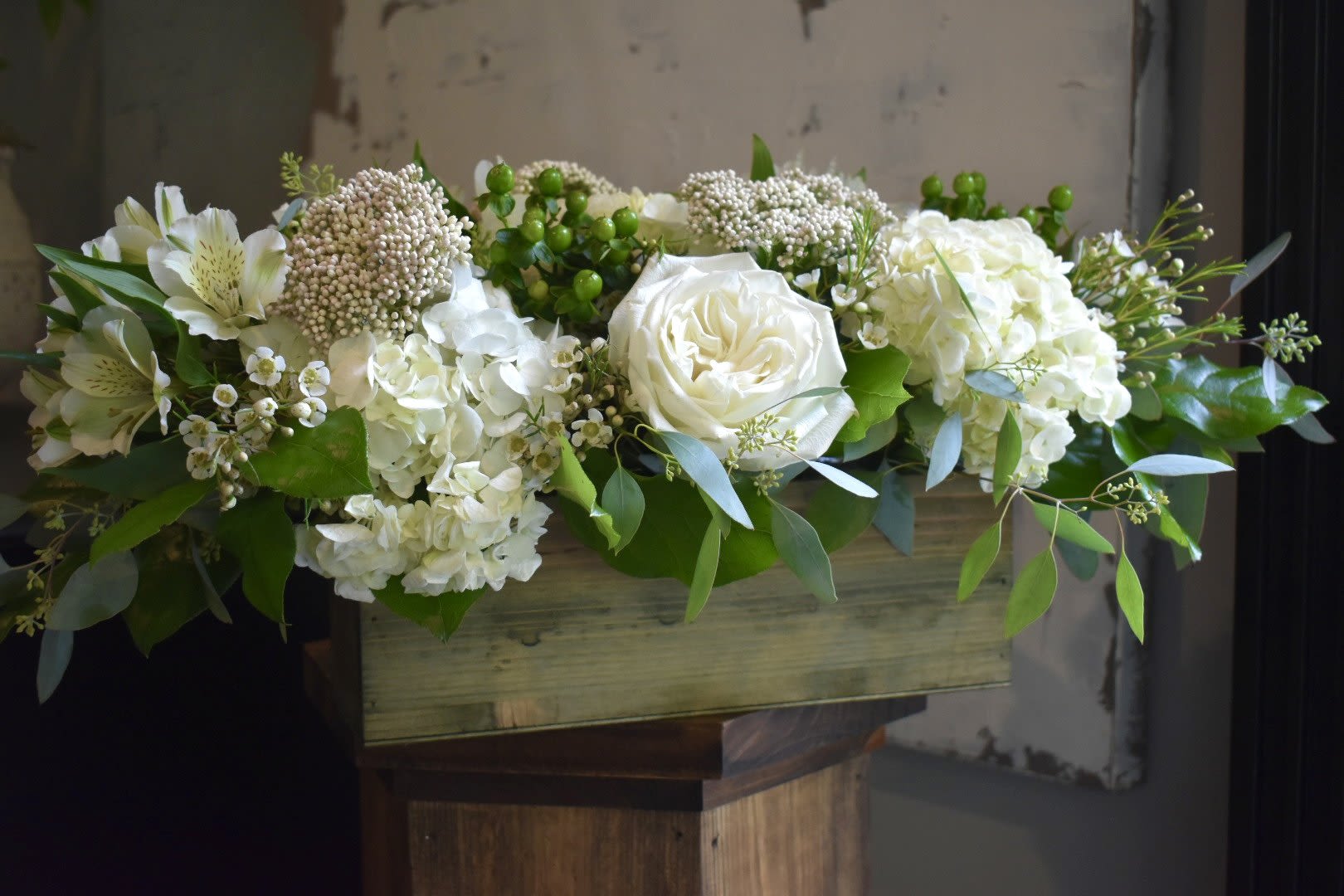 White floral arrangement in a wooden box with greenery
