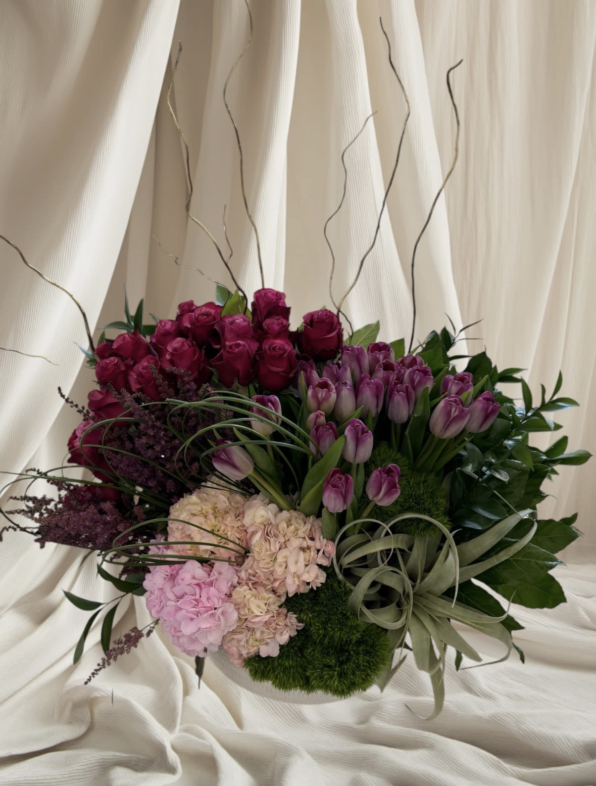 Bouquet of purple roses, tulips, and hydrangeas with decorative grasses