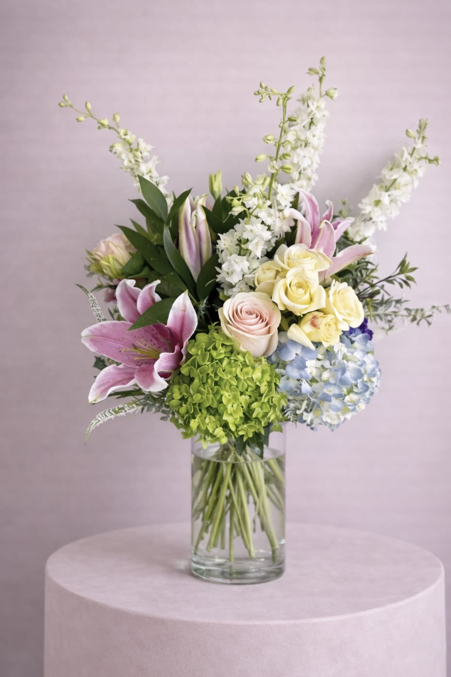 Mixed bouquet of lilies, roses, hydrangea, and white spikes in a glass vase