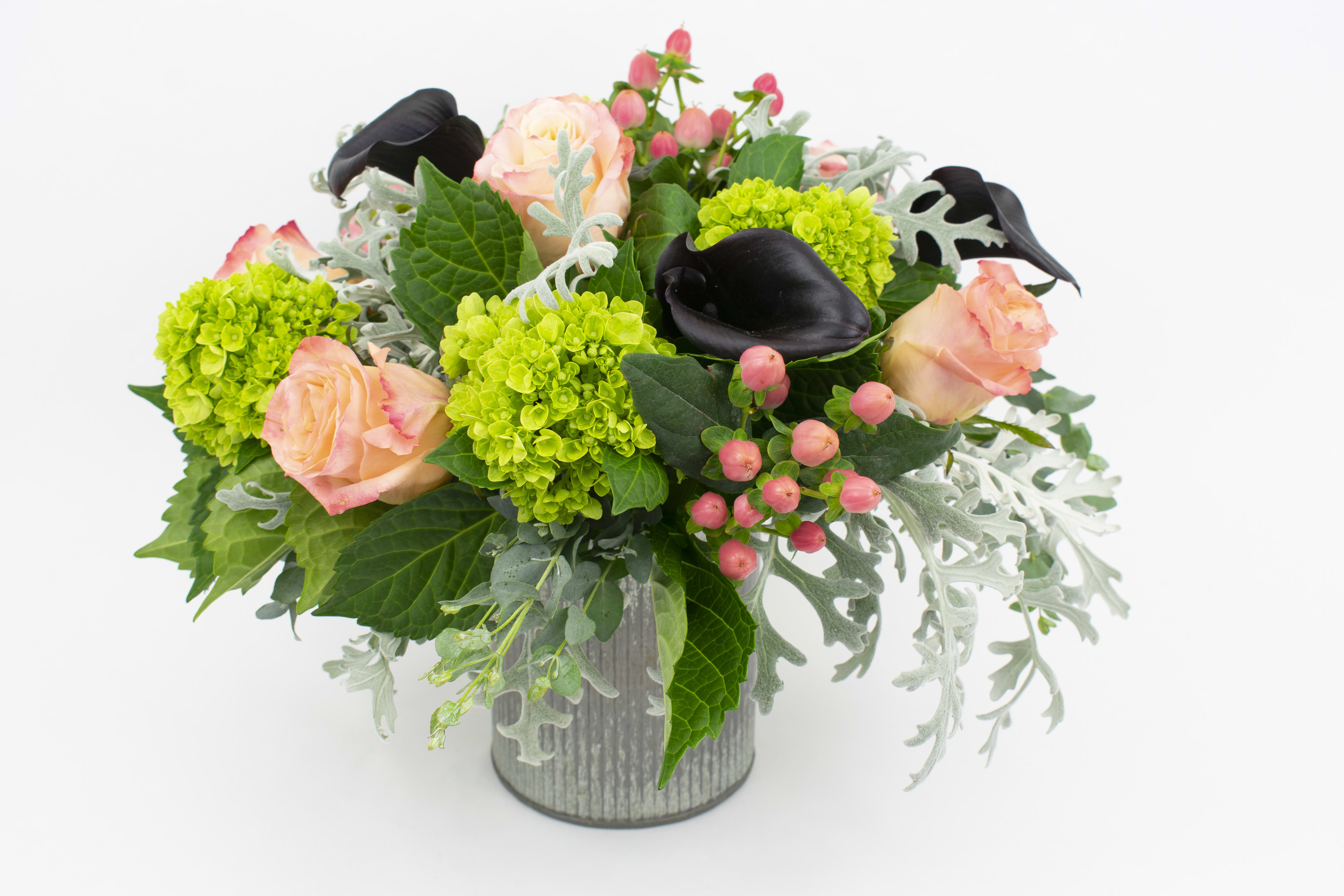 Bouquet of peach roses, green hydrangeas, and black calla lilies in a gray vase