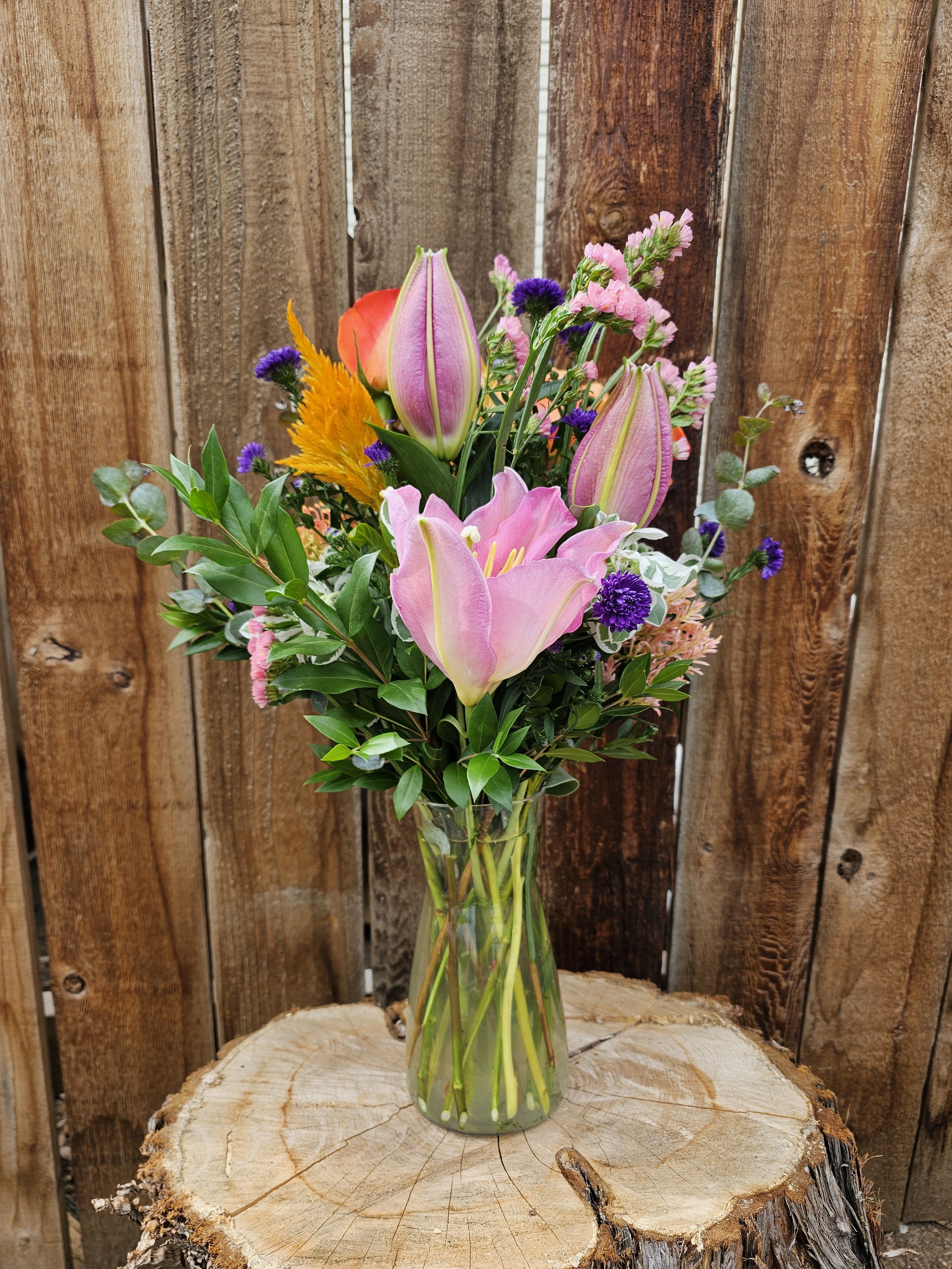 Pink lilies and mixed flowers arranged in a clear glass vase