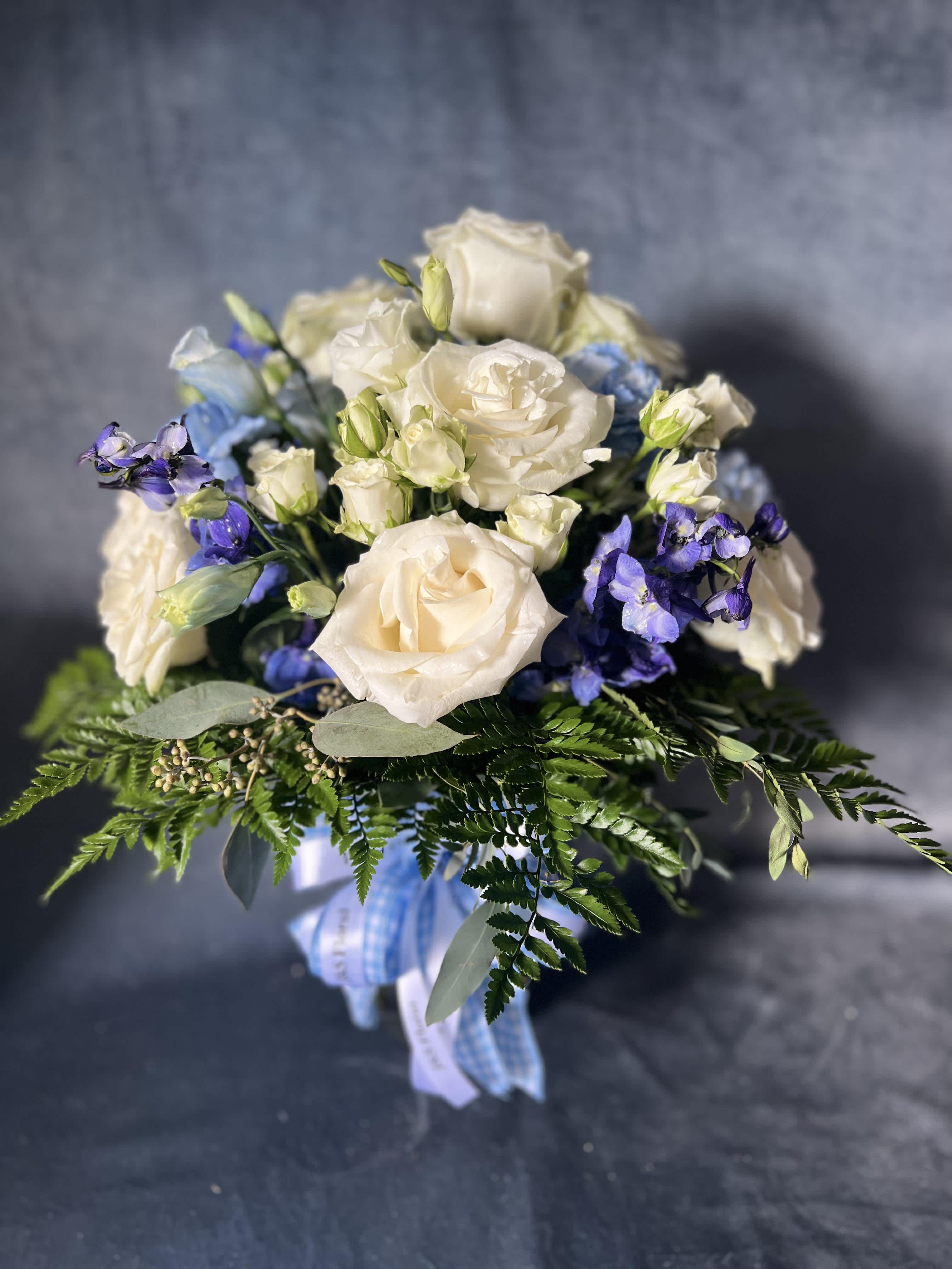 White roses and blue flowers in a hand-tied bouquet with ribbon