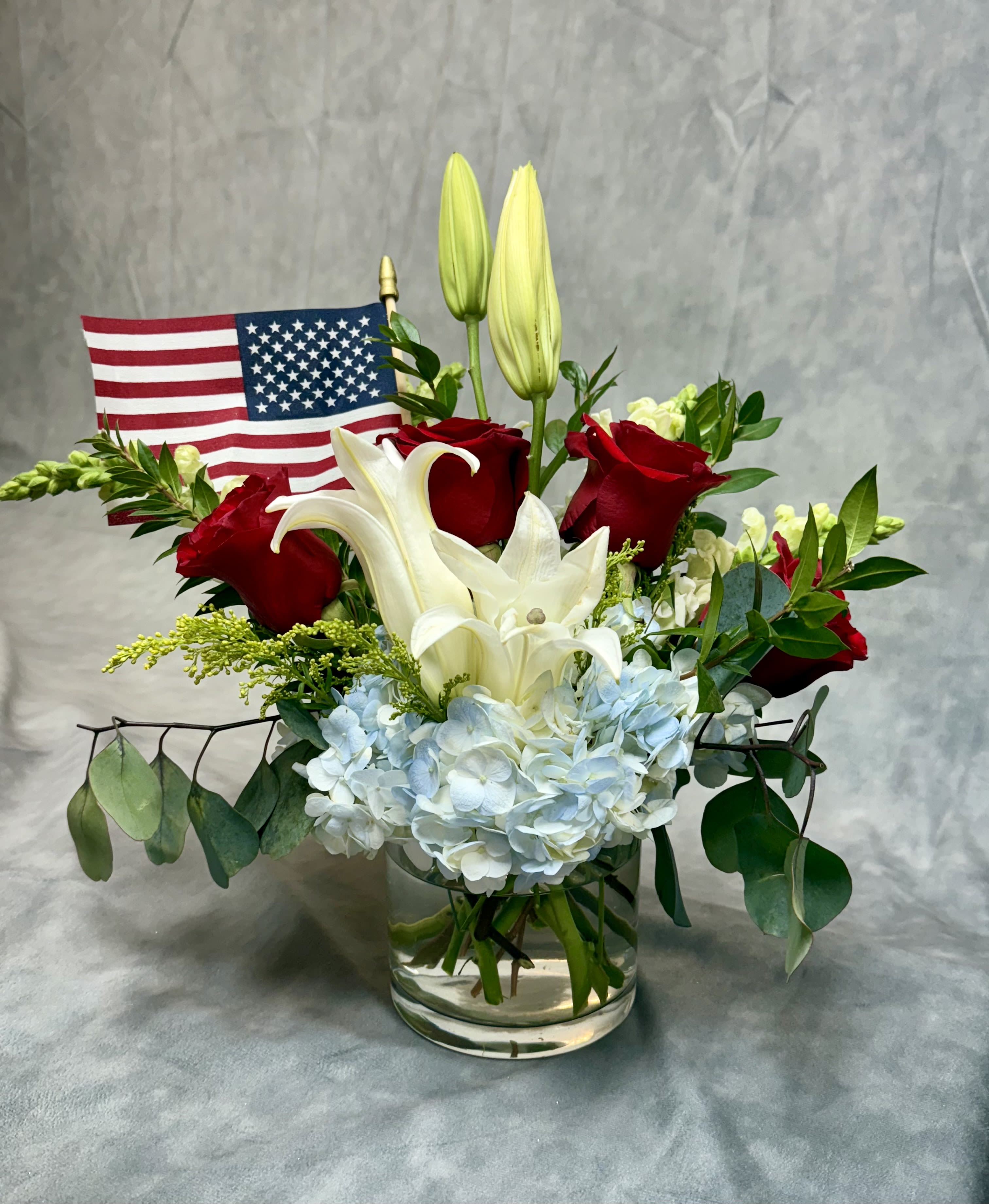 Red roses and white lilies in a glass vase with a small American flag