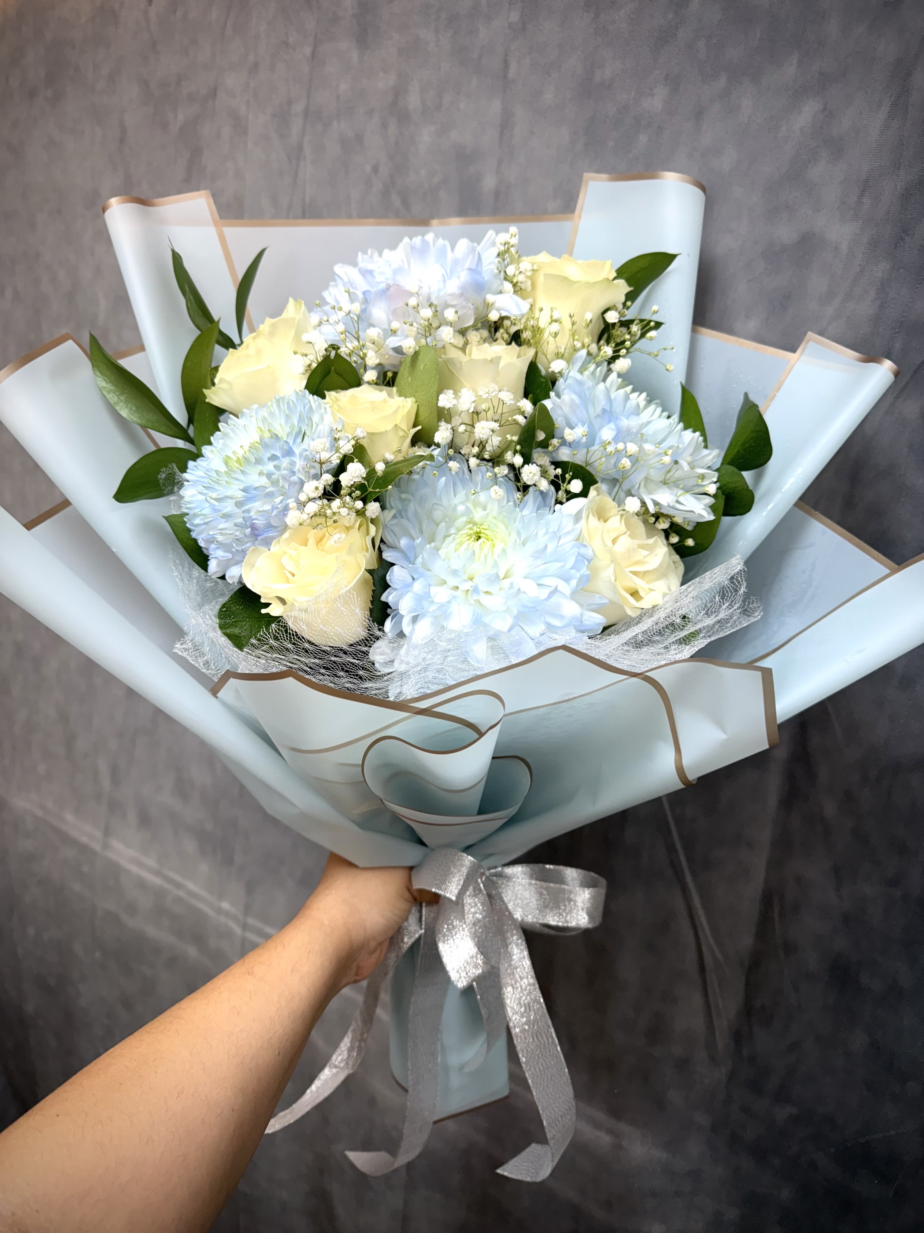 Bouquet of pale blue chrysanthemums and cream roses wrapped in light blue paper