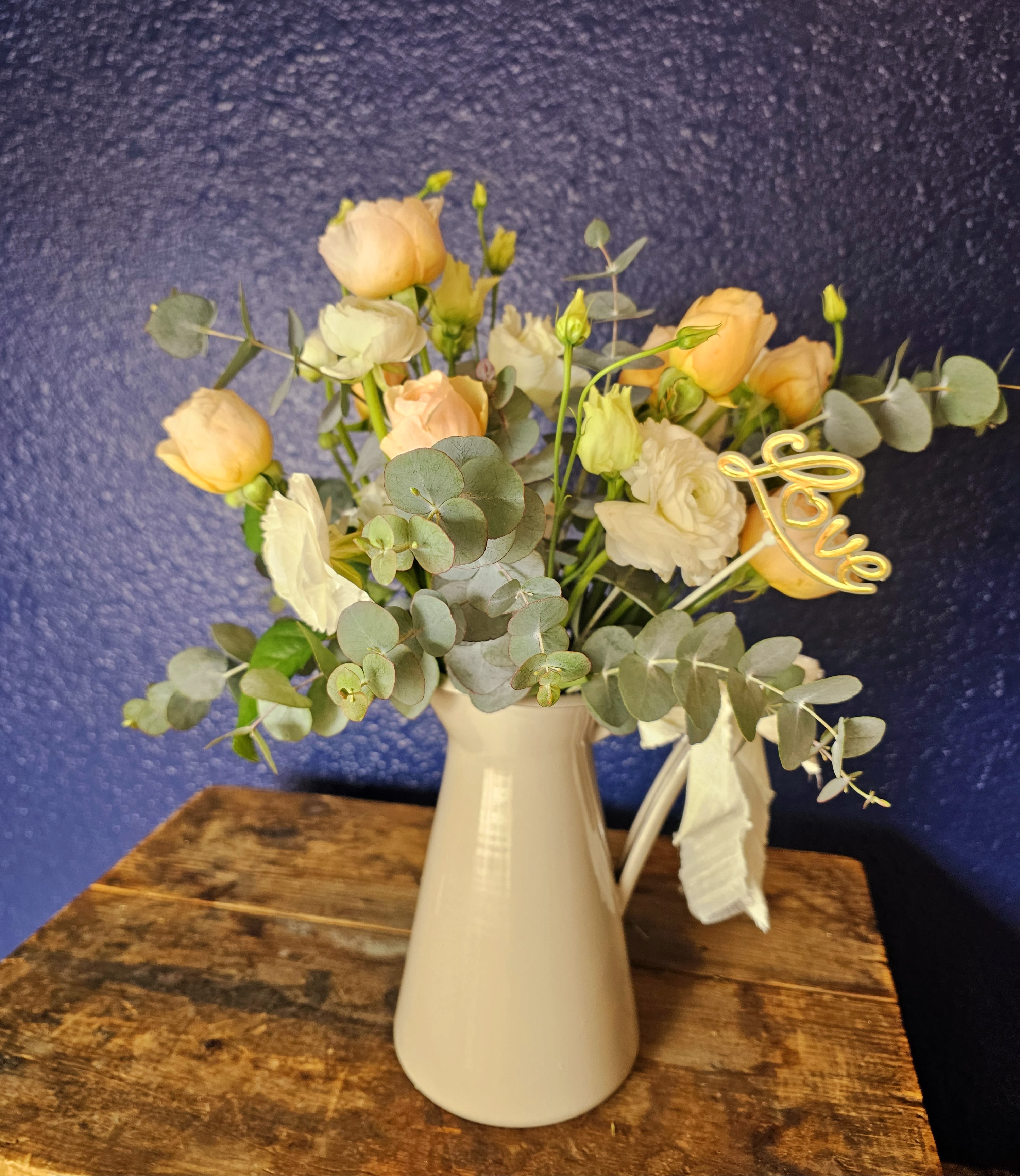 Peach and white flowers in a white vase with eucalyptus and a gold "love" pick