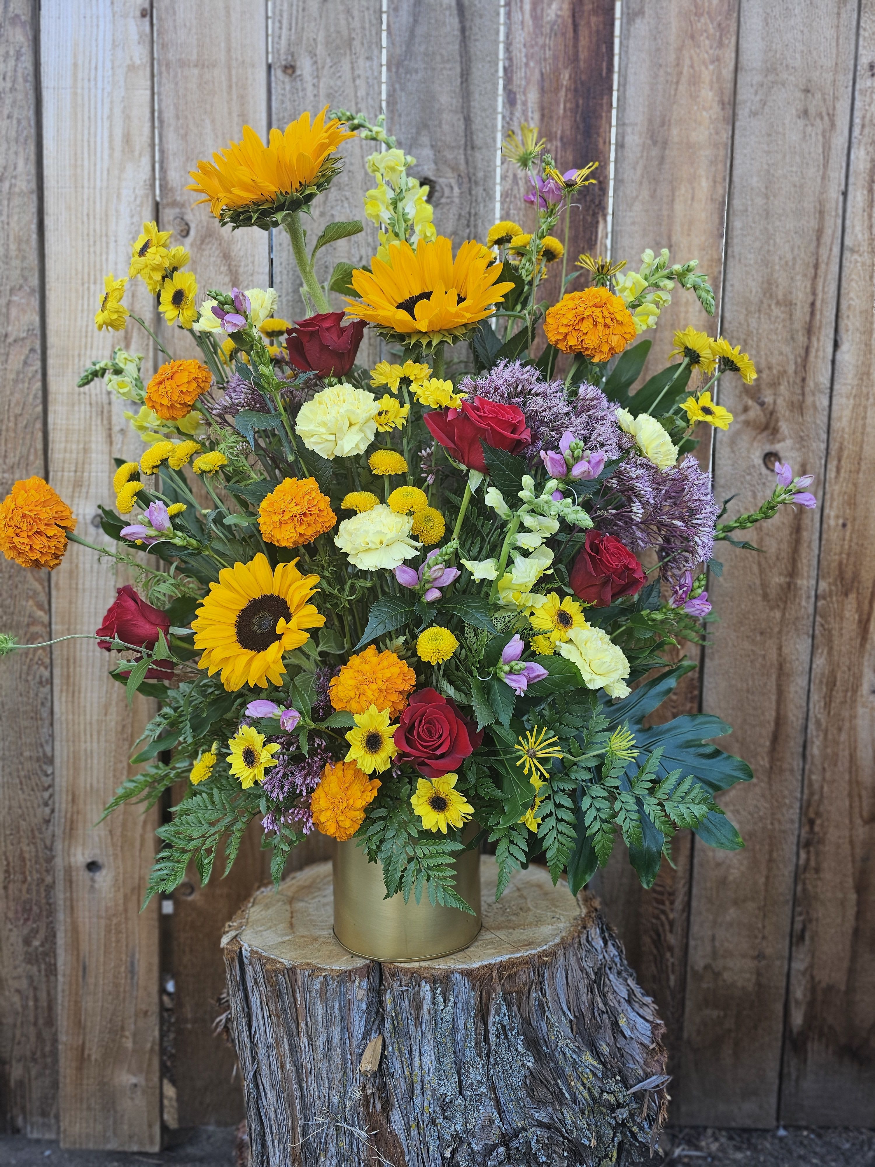 Mixed bouquet of sunflowers, roses, and marigolds in a gold vase