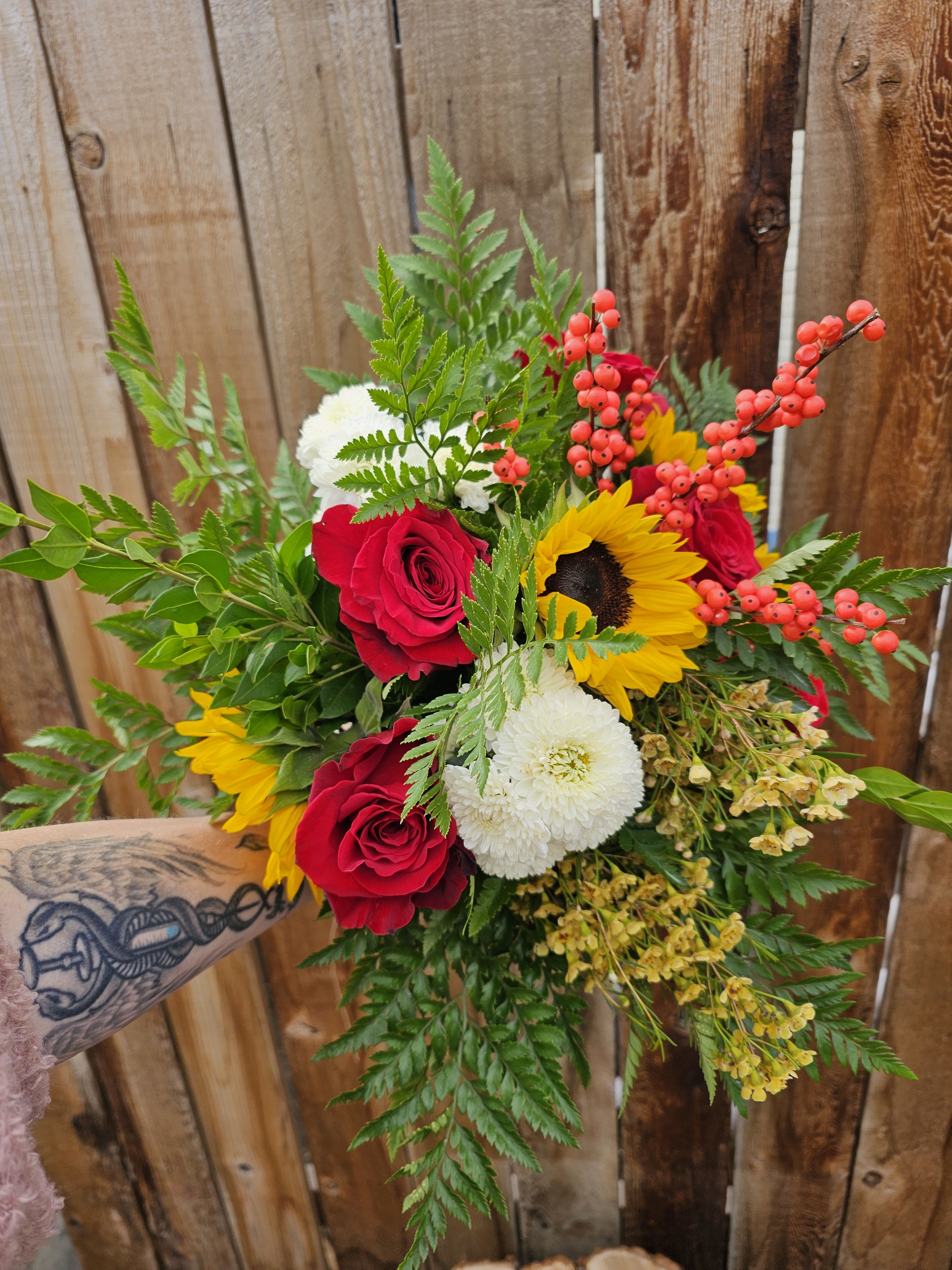 Bouquet of red roses, sunflowers, and white mums with berry accents