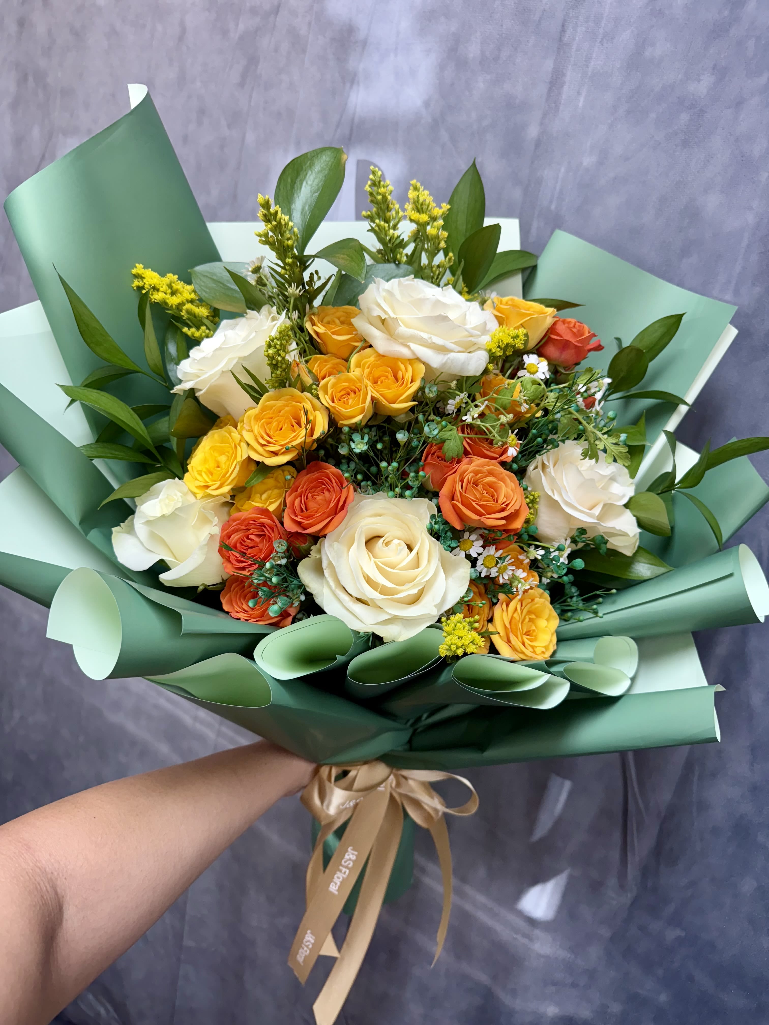 Bouquet of white, yellow, and orange roses wrapped in green paper
