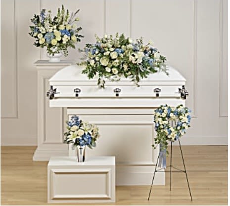 White casket with blue and white floral sprays in a funeral room