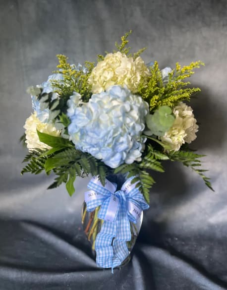 Blue and white hydrangea bouquet in a glass vase with a blue ribbon