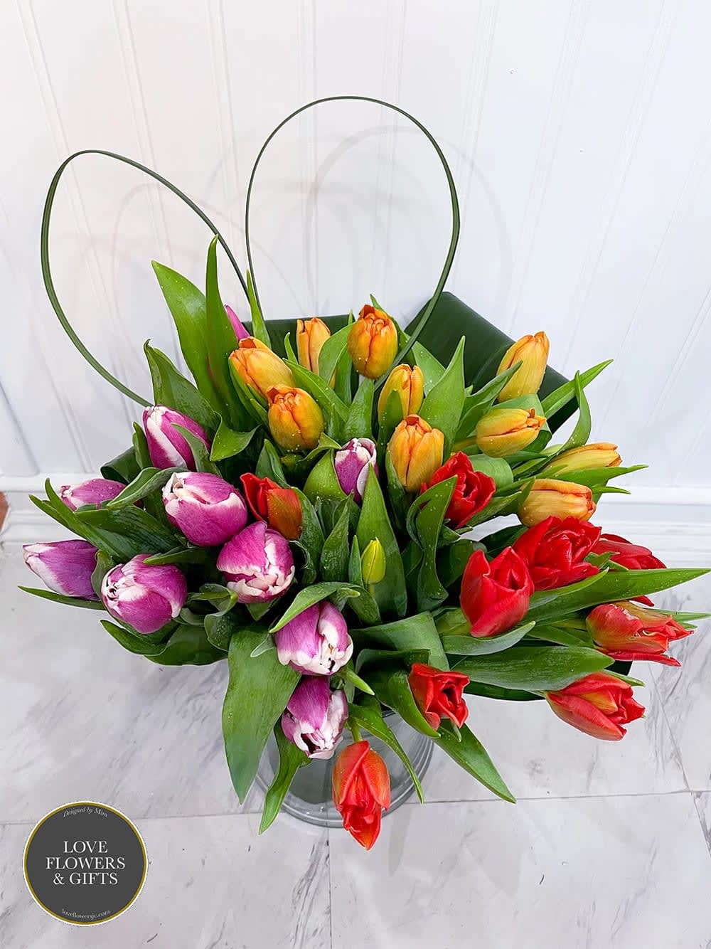Multicolored tulip arrangement with orange, red, and purple blooms in a clear glass vase