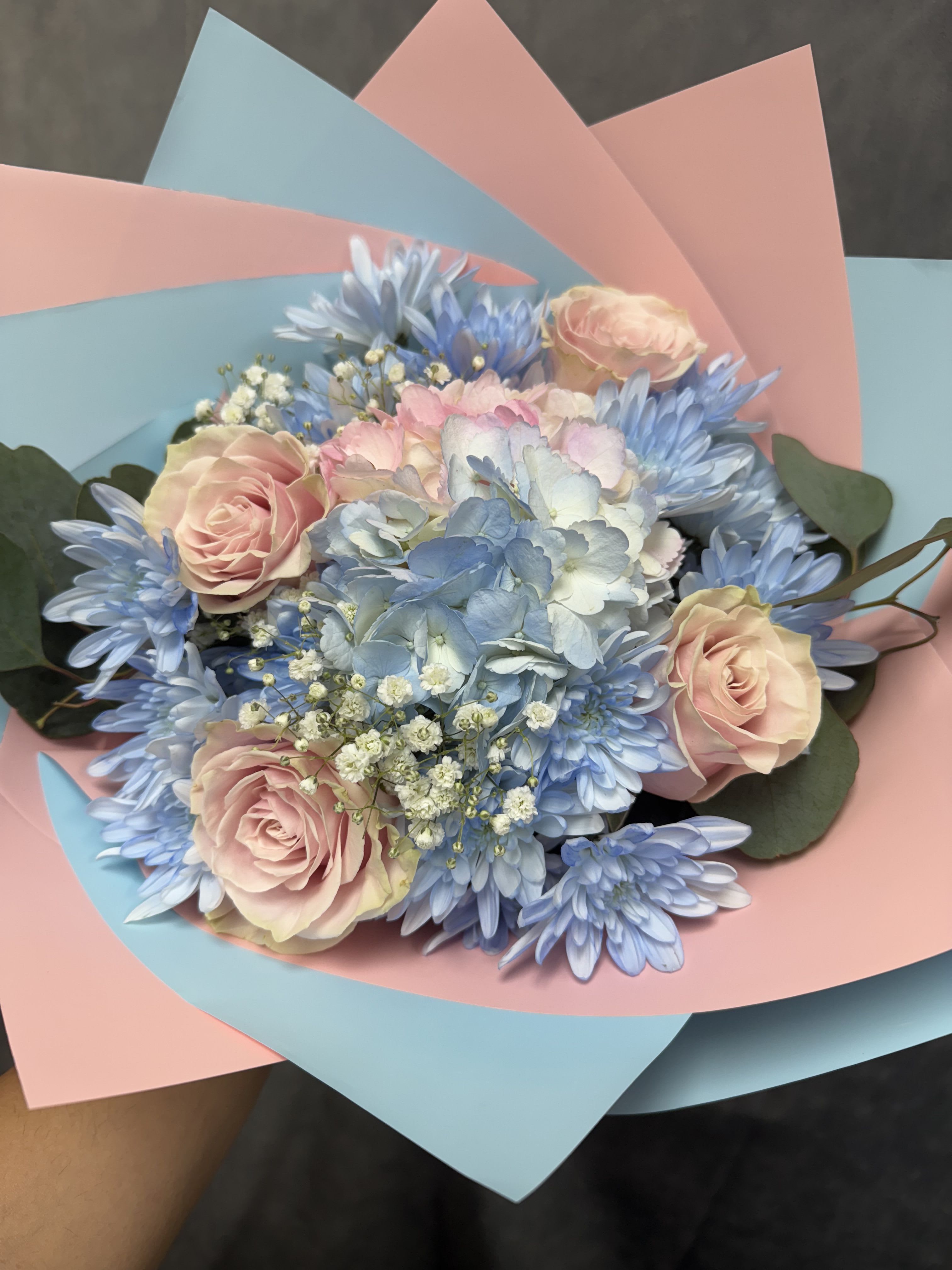 Bouquet of pale pink roses and blue flowers wrapped in pink and blue paper