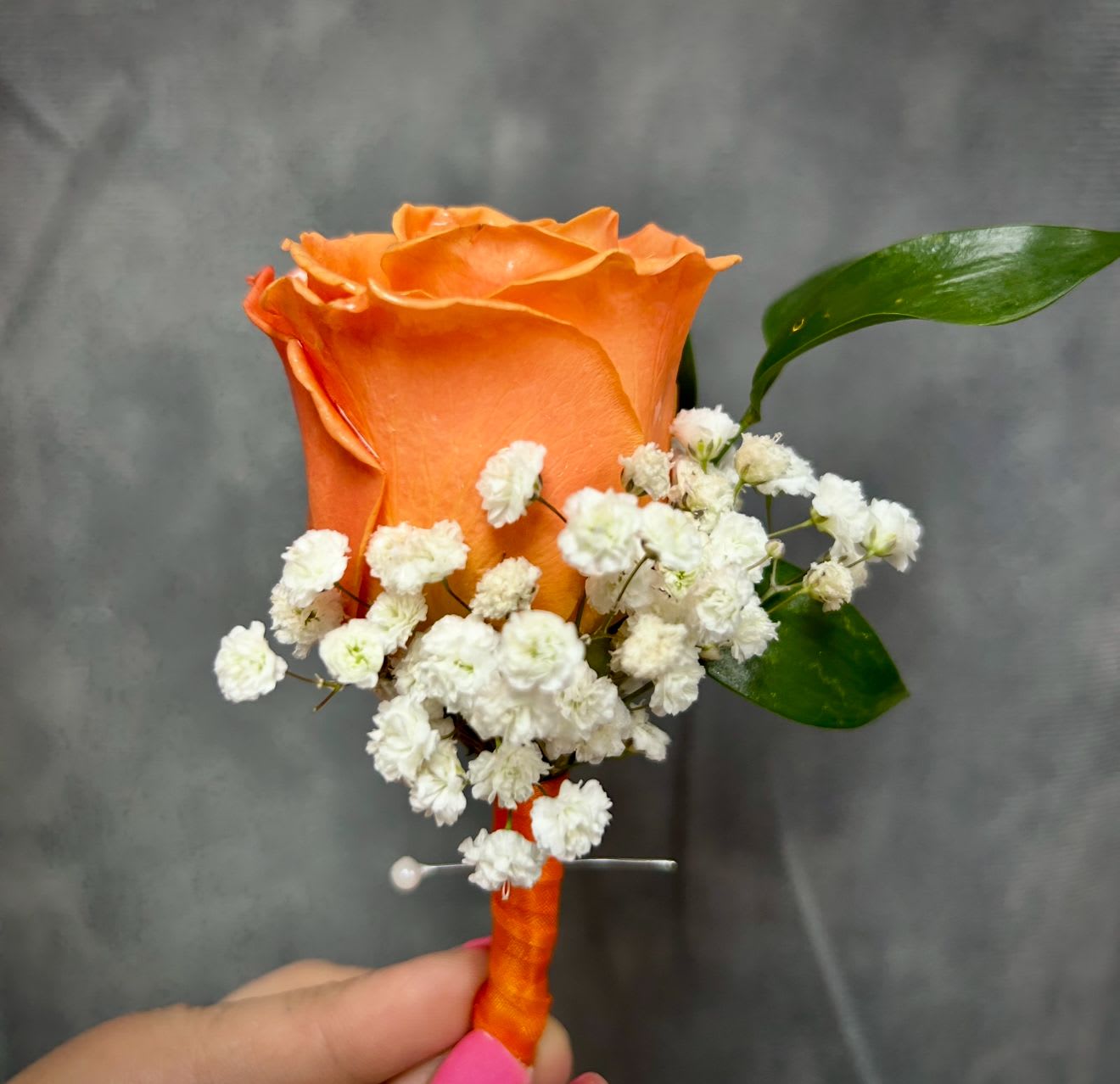 Orange rose boutonniere with white baby's breath and green leaves