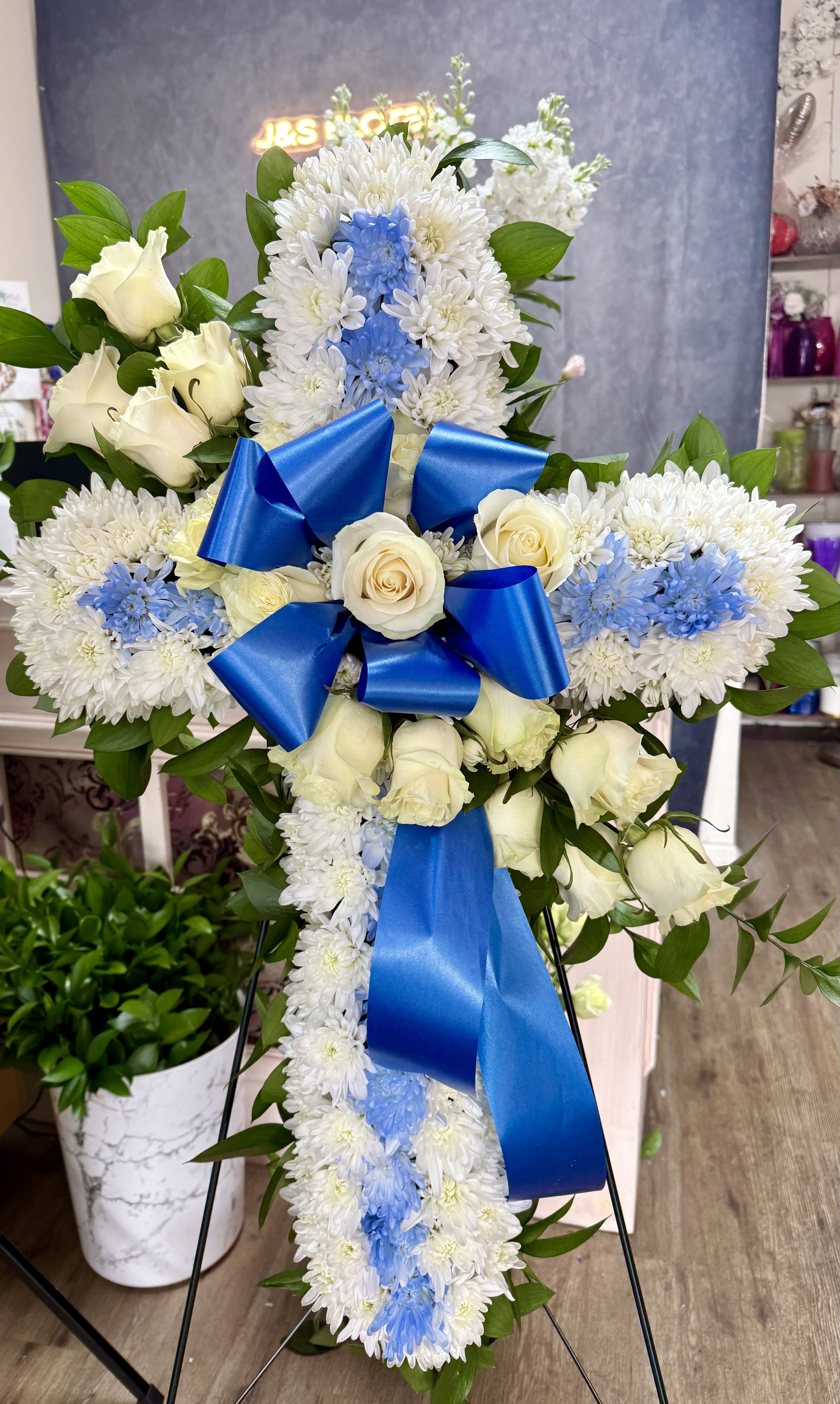 White floral standing cross with blue ribbon and roses