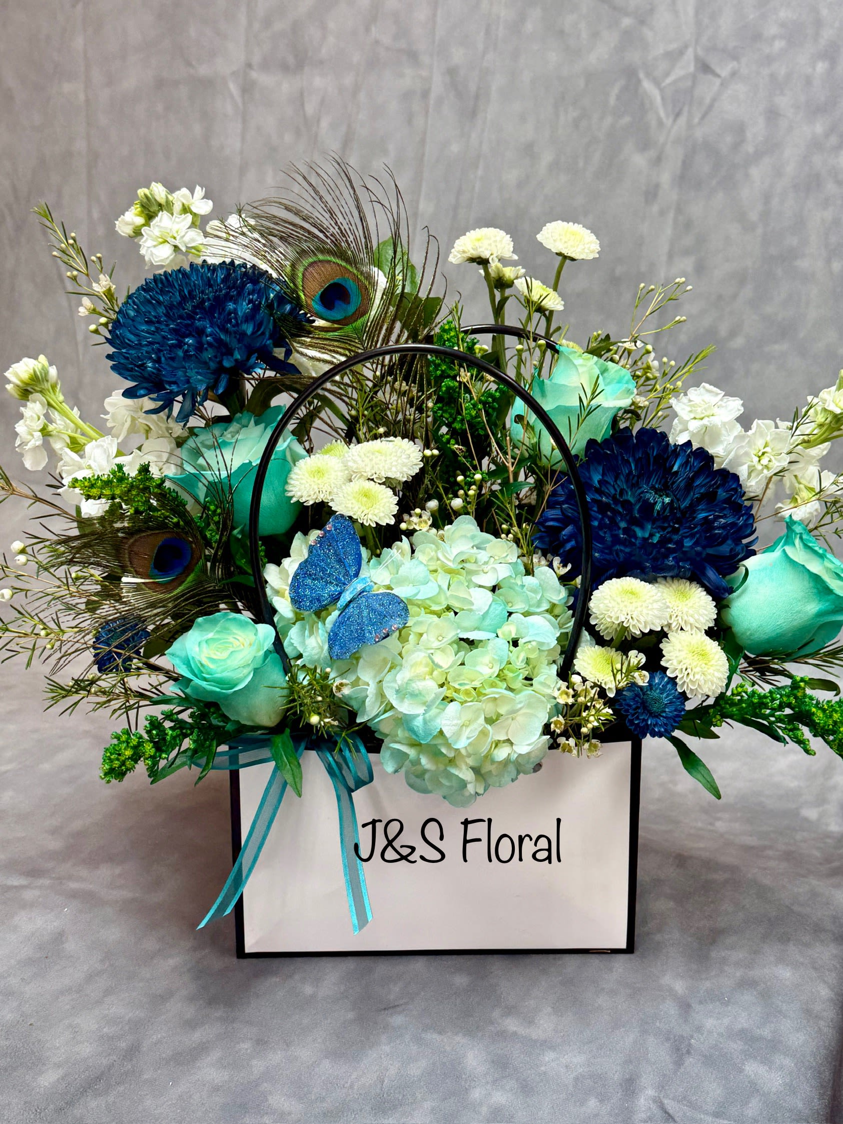 Blue and white floral arrangement in a white gift box with peacock feathers