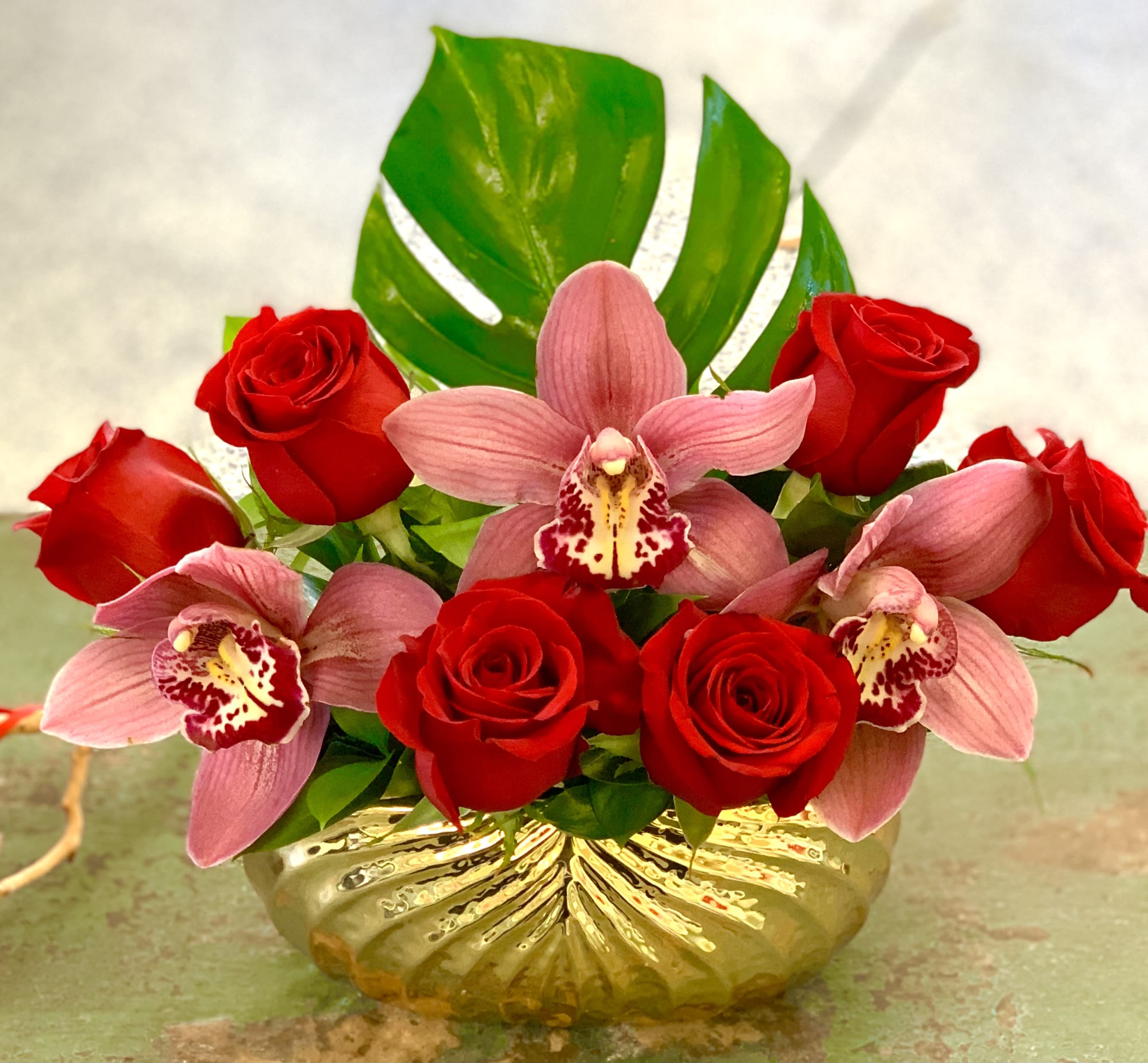 Red roses and pink orchids arranged in a gold vase