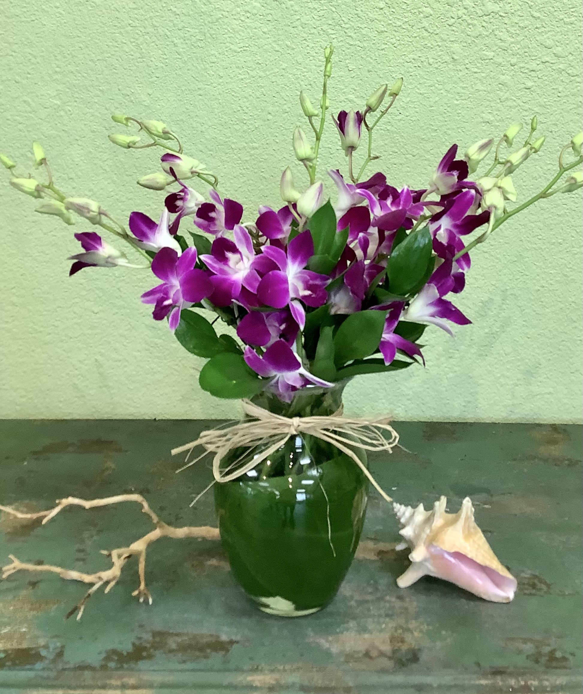 Purple orchids arranged in a green glass vase with a raffia bow