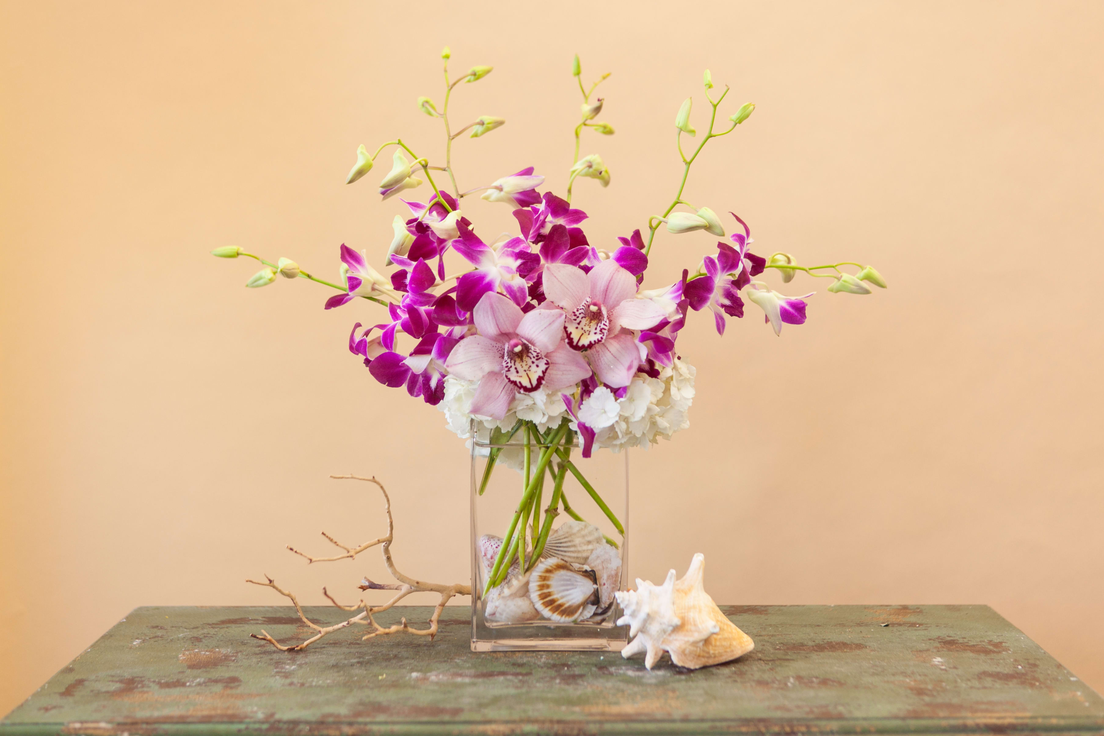 Pink and purple orchids in a clear glass vase with seashells