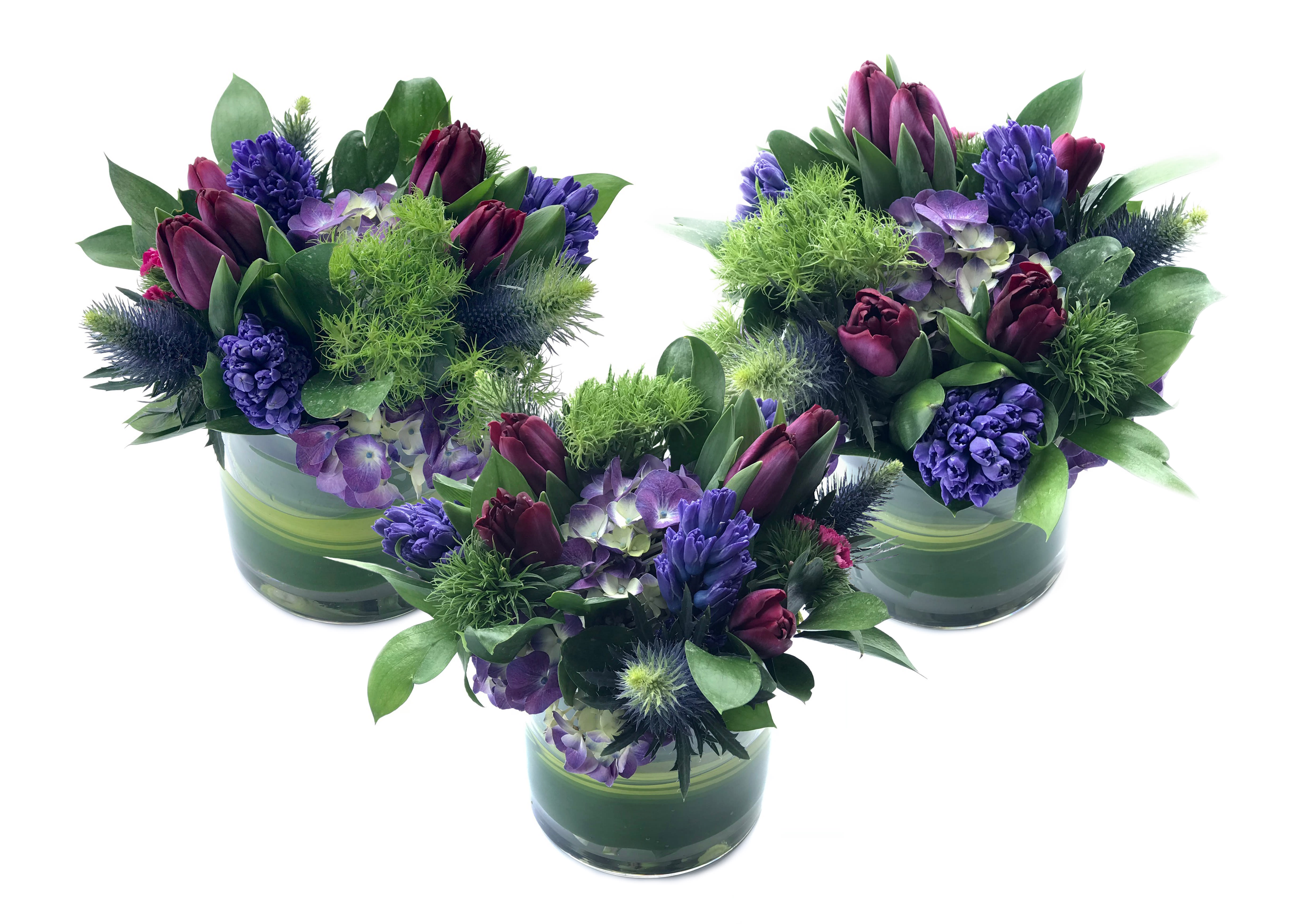 Three purple floral arrangements in green glass vases