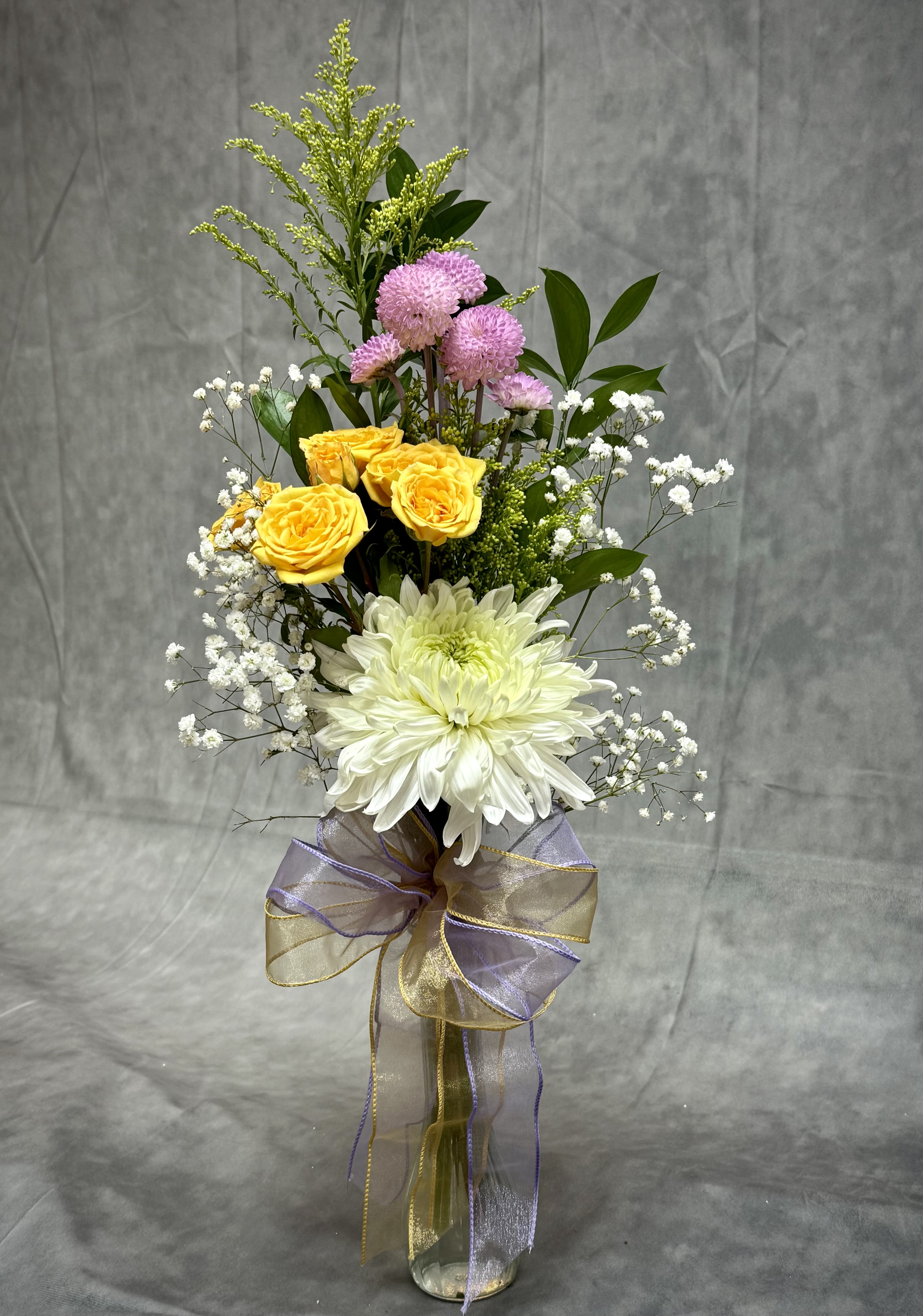 Tall bouquet of yellow and white flowers in a glass vase with a ribbon bow