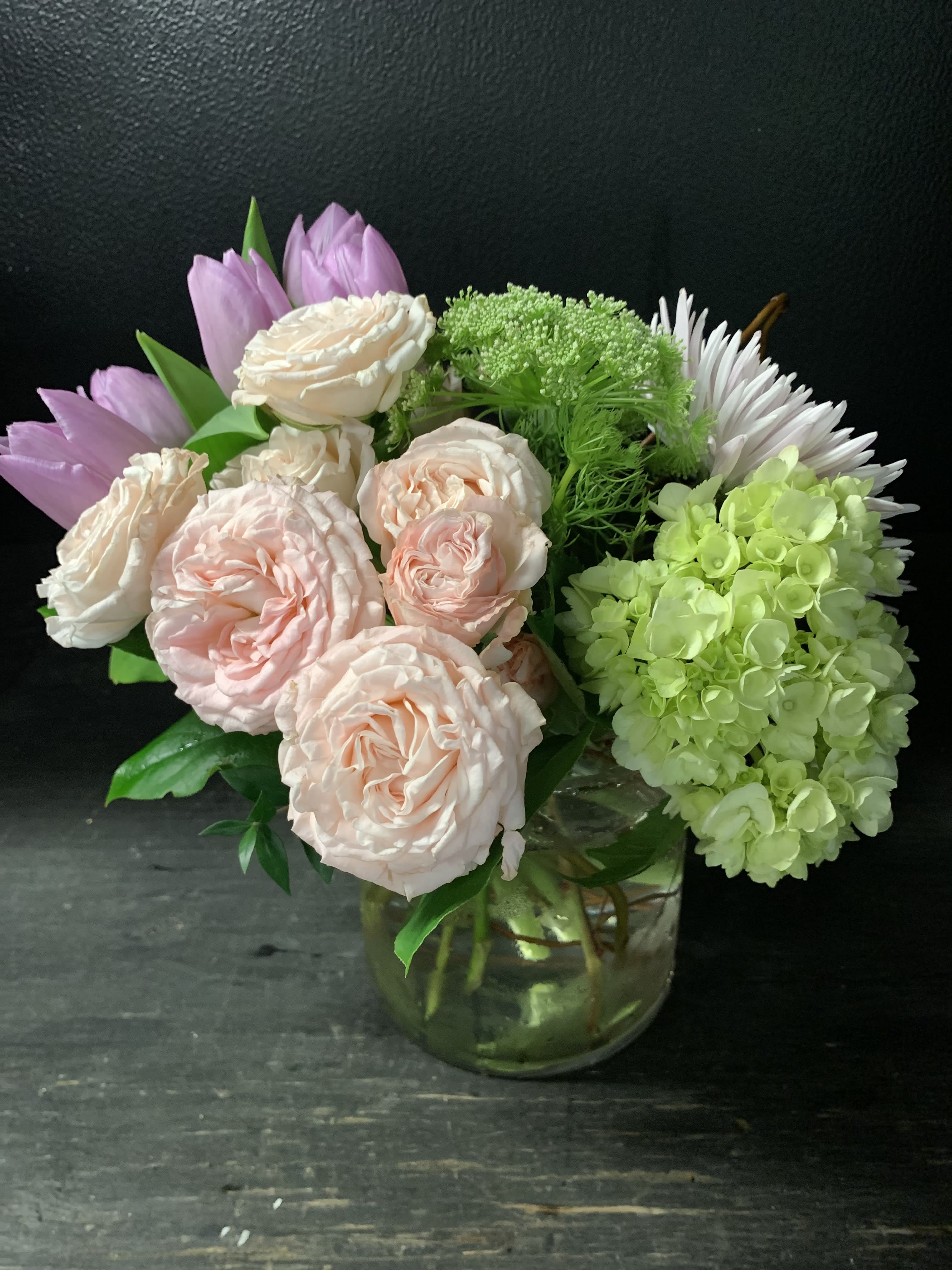 Mixed bouquet of pale pink roses, green hydrangea, and white daisies in a glass vase