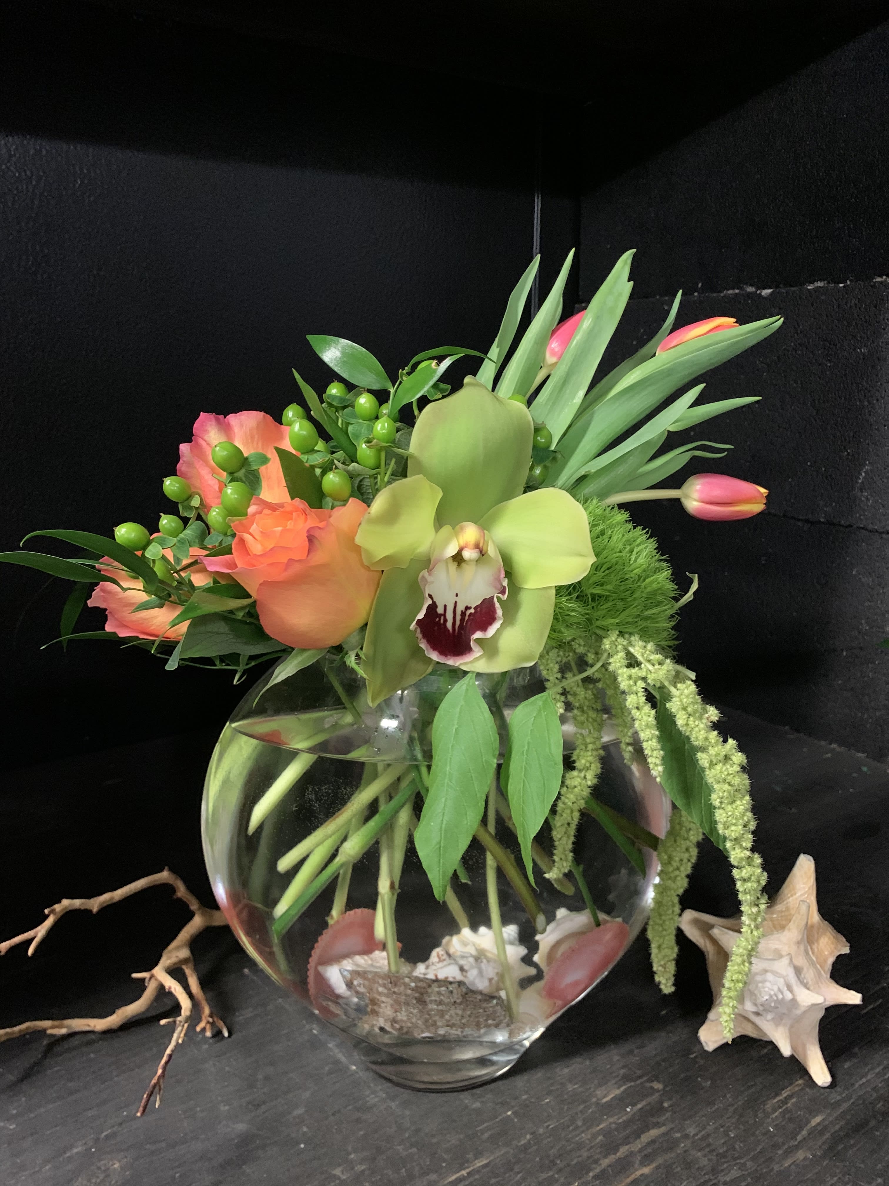 Tropical floral arrangement in a round glass vase with orchids and tulips